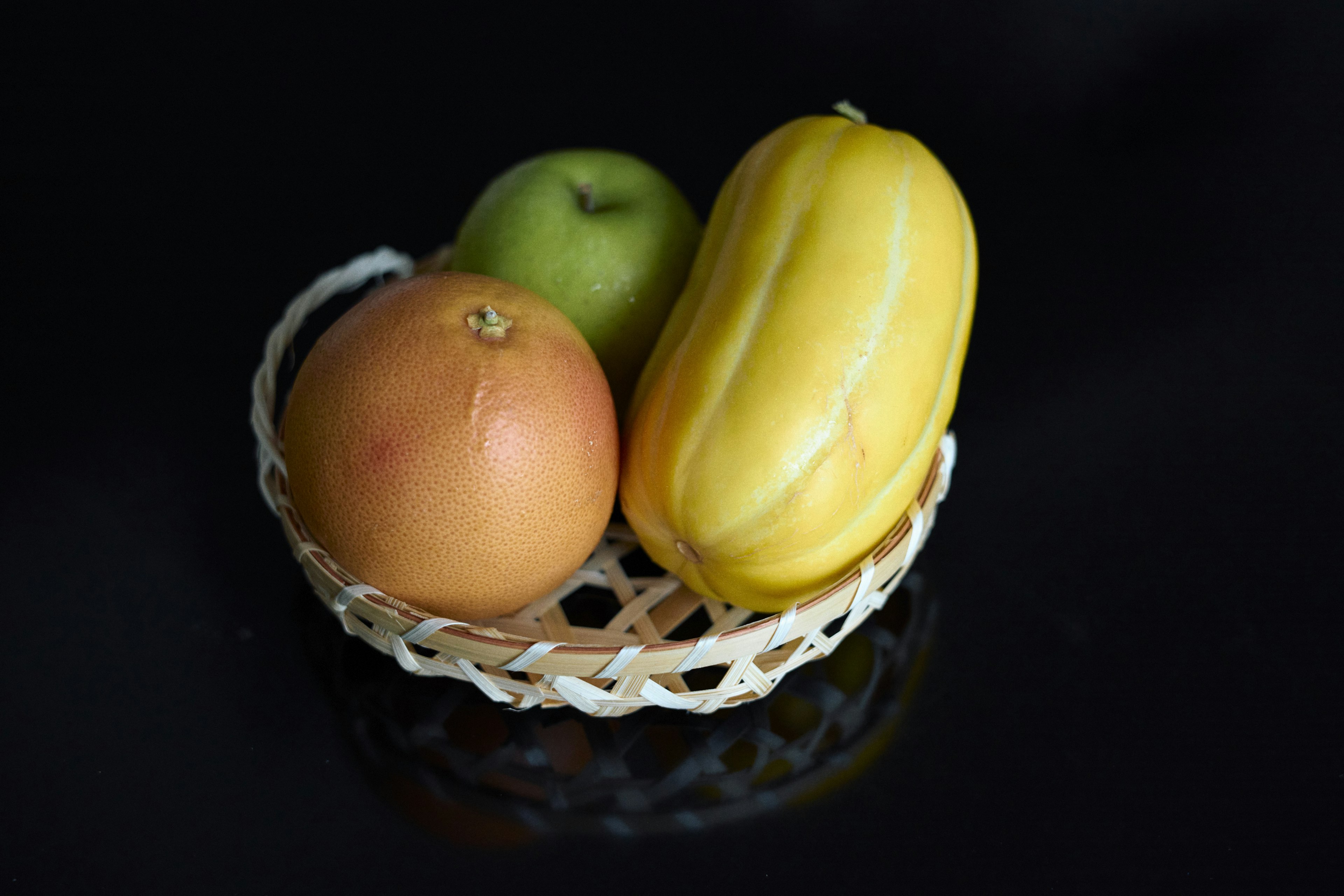 Un panier contenant un fruit jaune une pomme verte et un fruit orange sur un fond noir