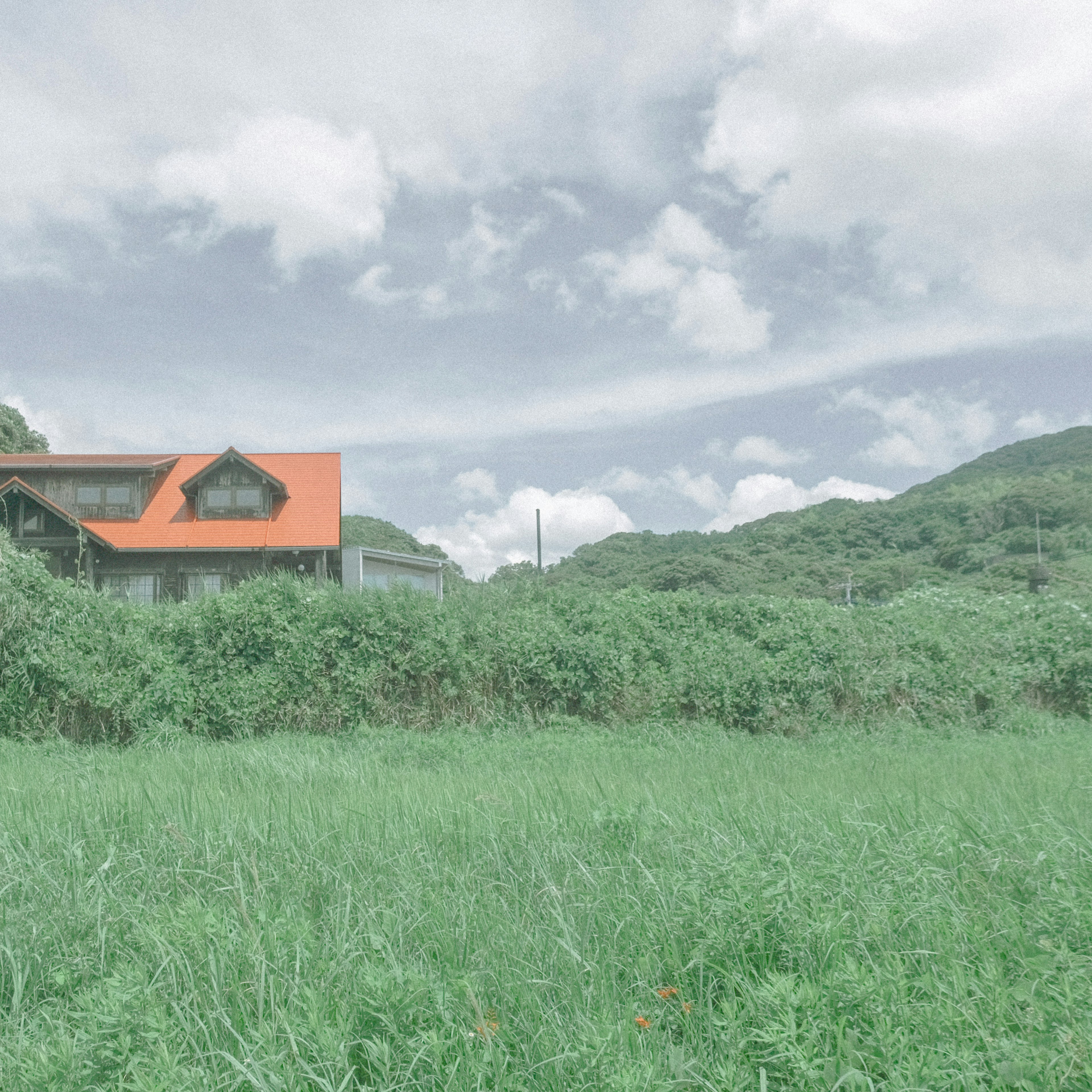 一座橙色屋頂的房子被綠色草地和小山環繞，天空多雲