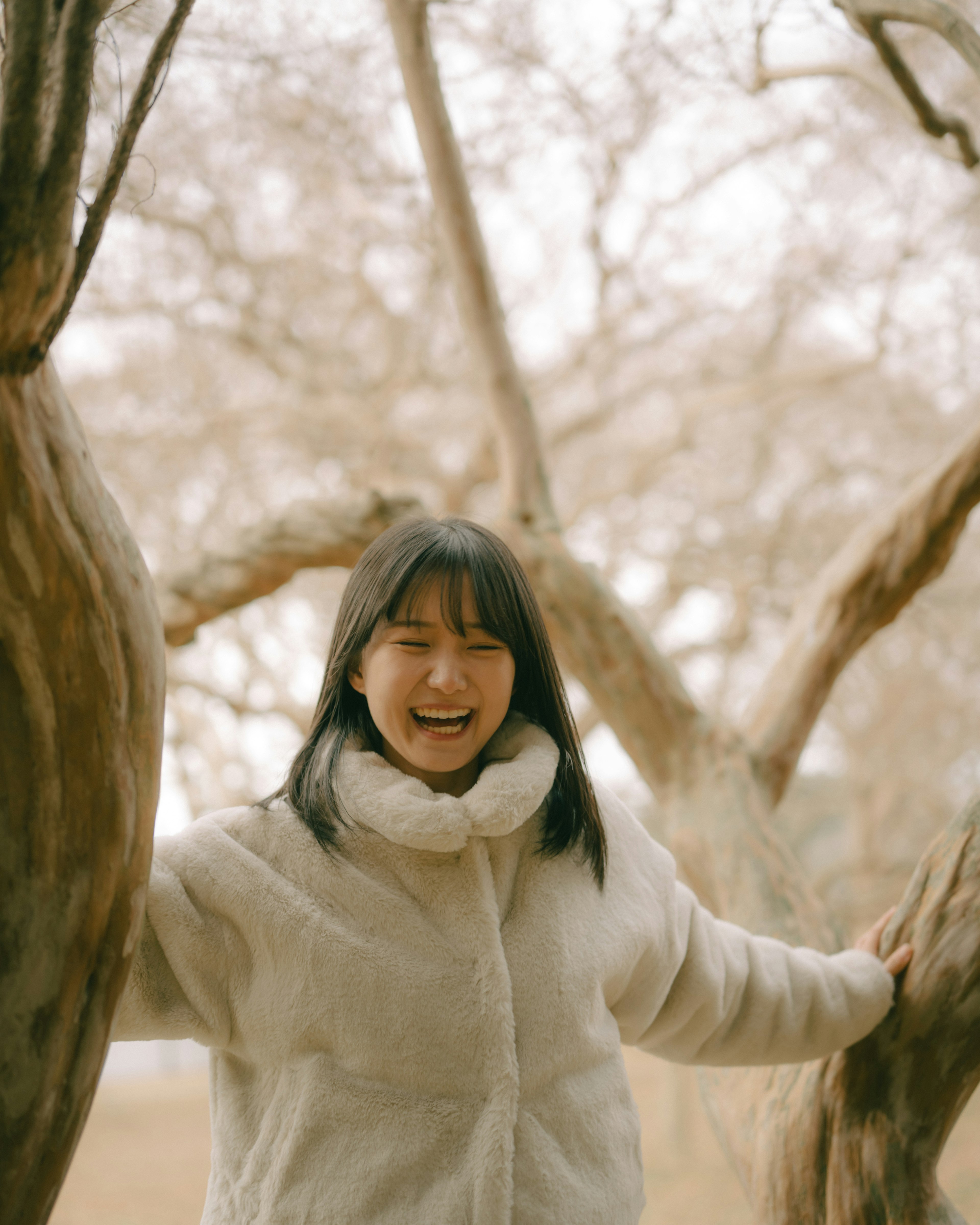 Smiling woman in a warm coat standing between trees enjoying nature