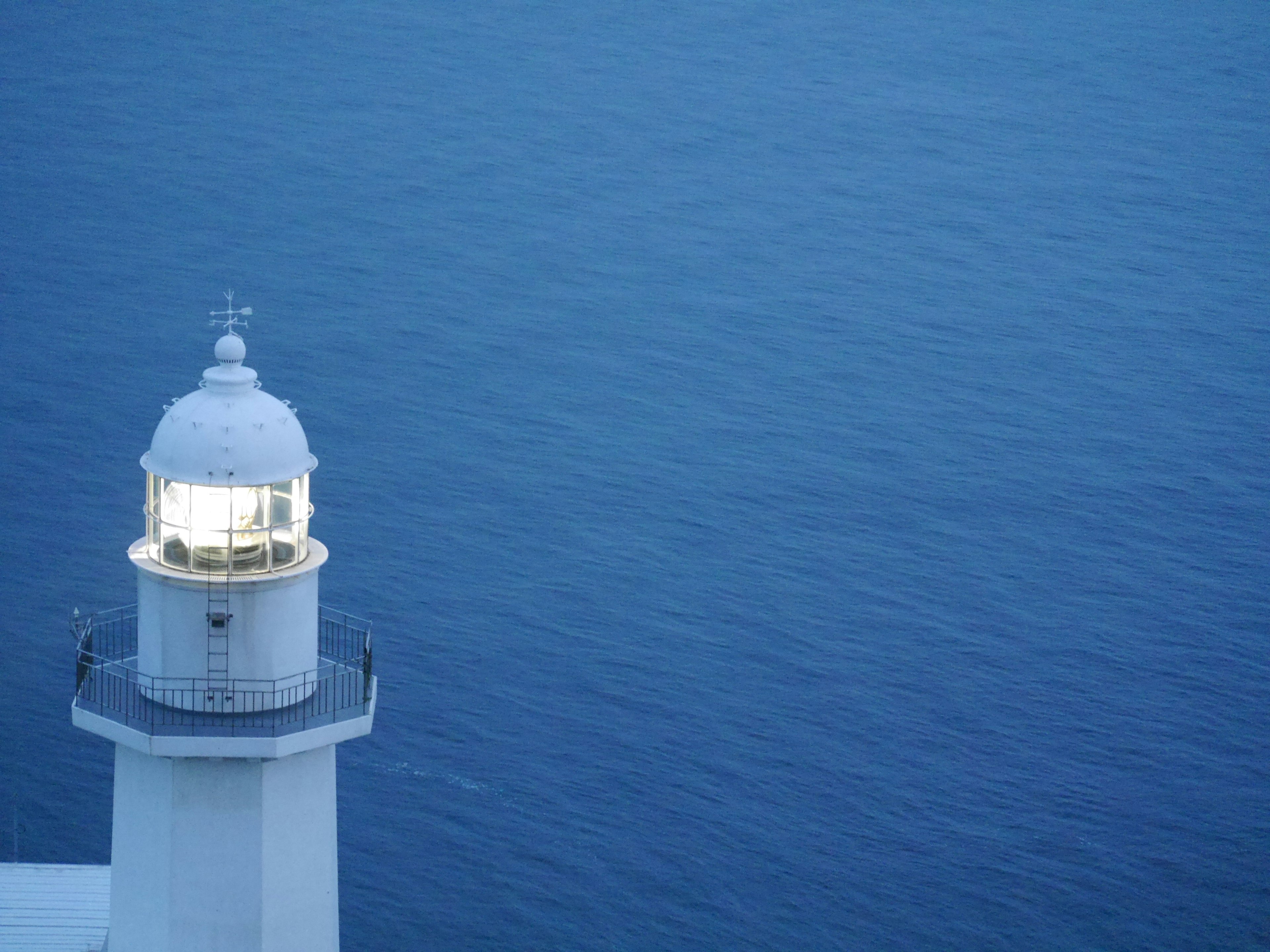 Top part of a white lighthouse standing over blue water