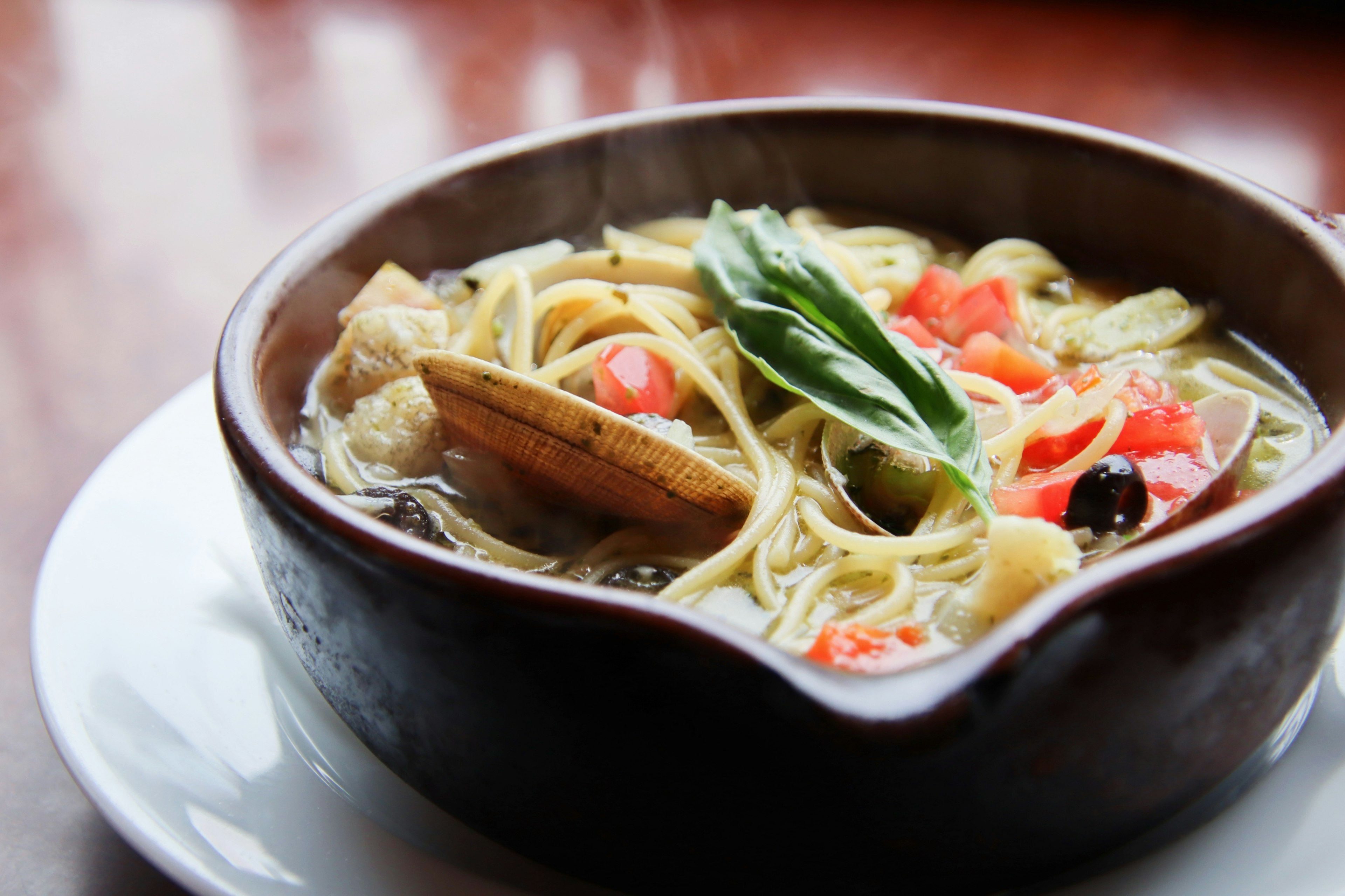 Mangkuk sup dengan pasta yang dihiasi tomat segar dan basil