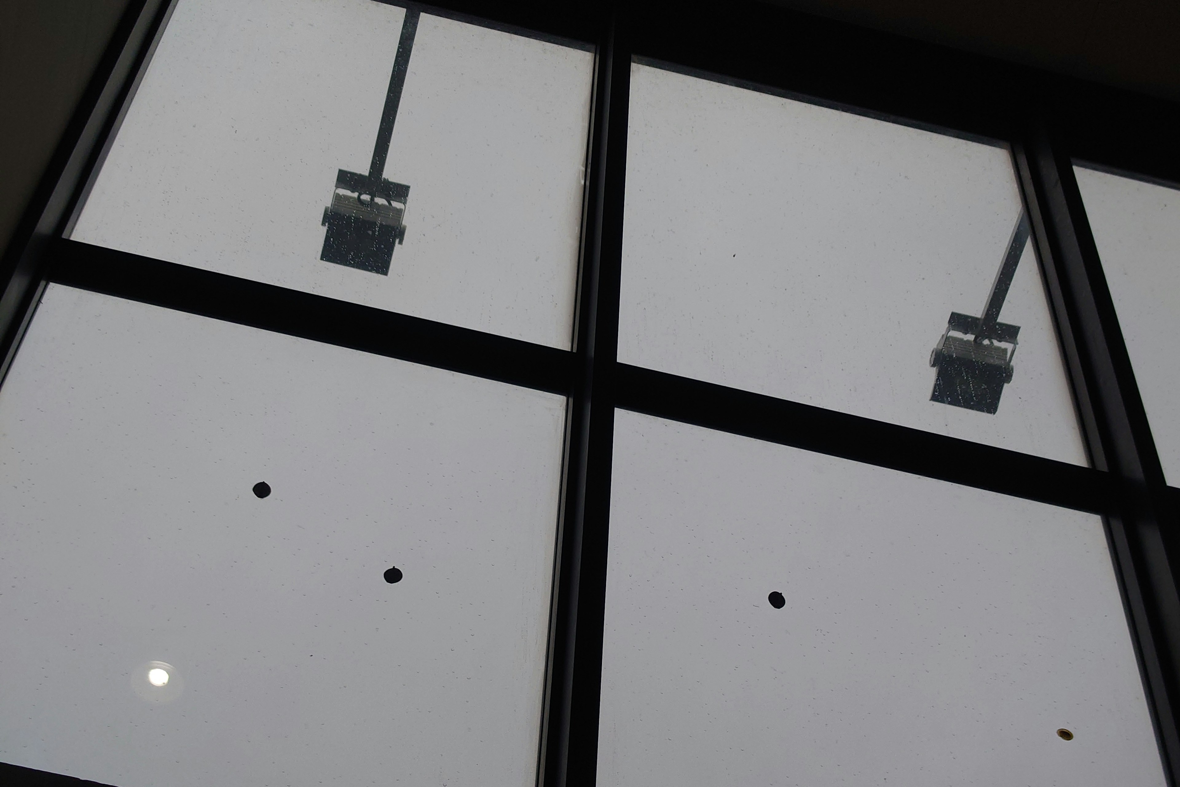 A photo of a window viewed from below showing ceiling lights and an overcast sky