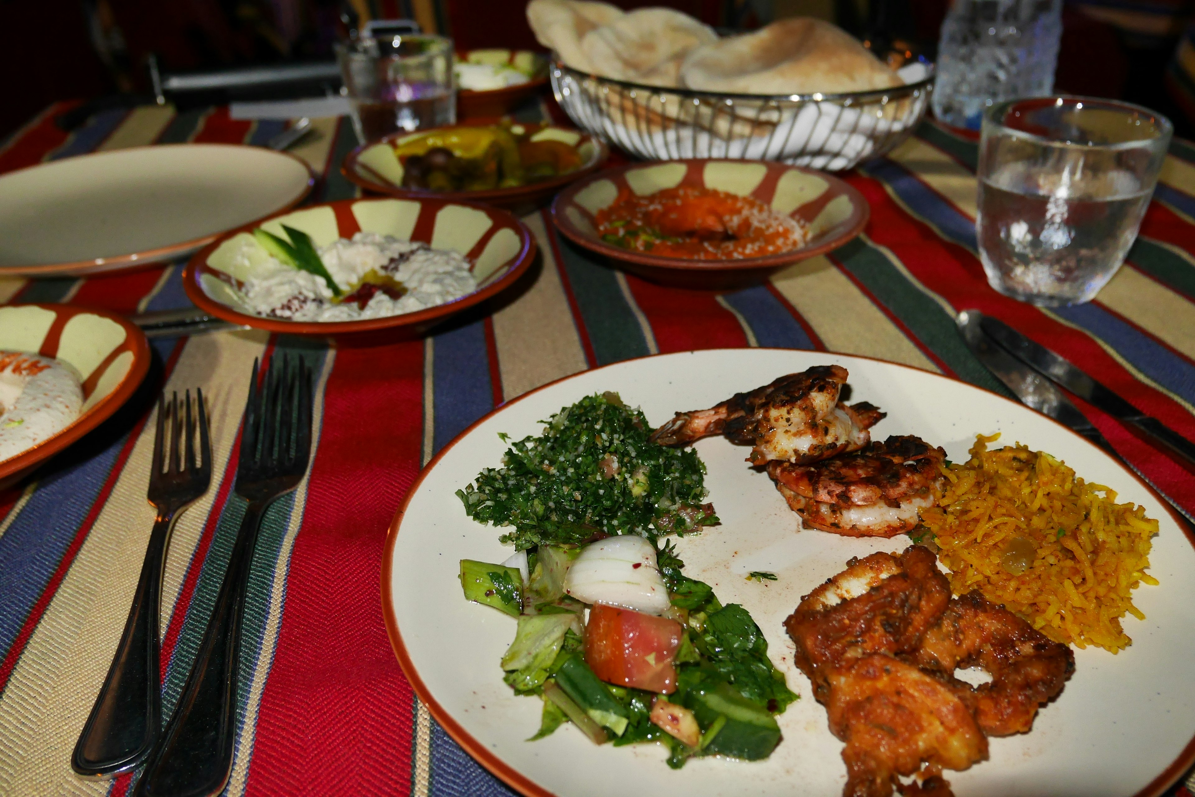 A plate of food featuring grilled shrimp salad and rice on a colorful striped tablecloth