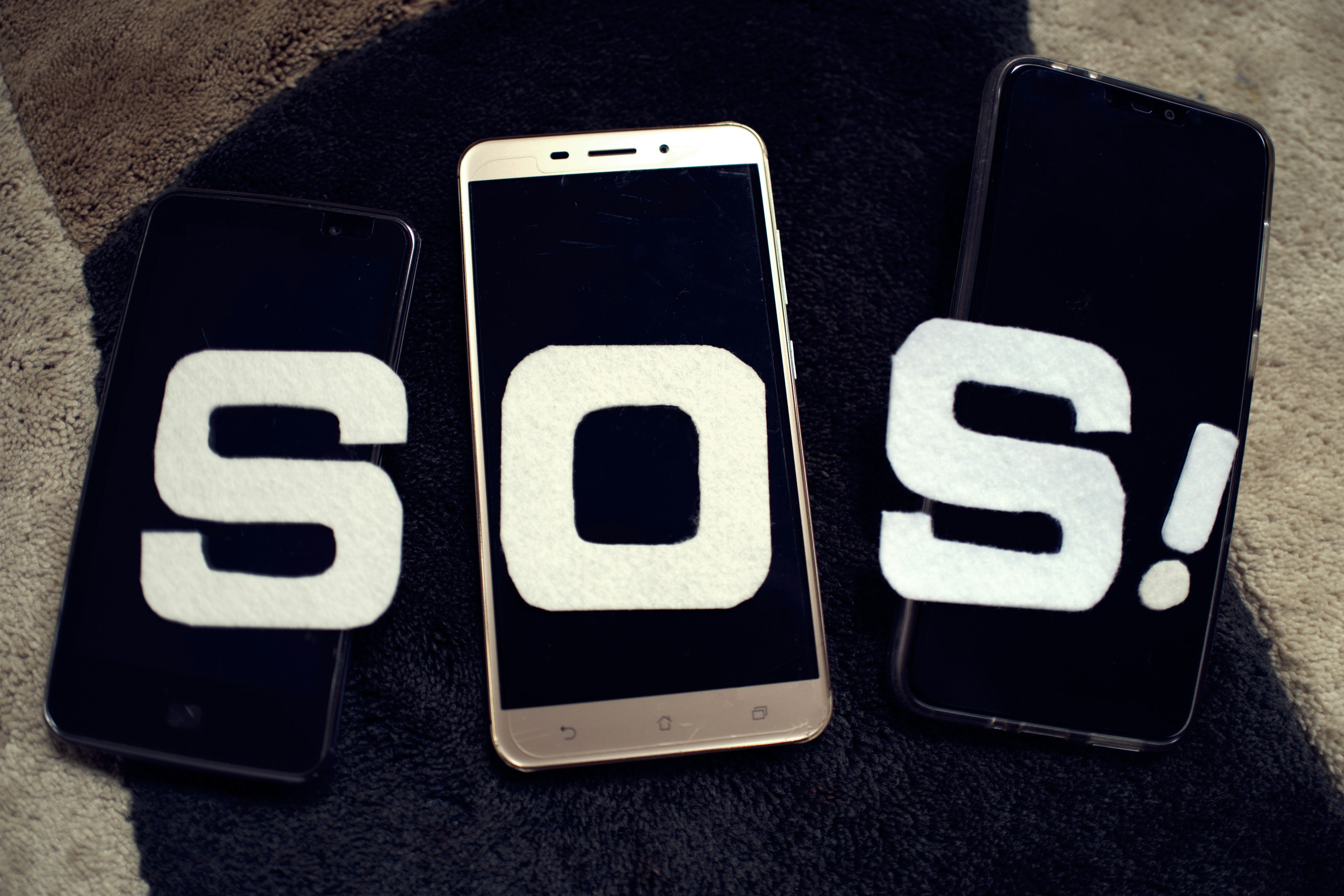 Three smartphones on a dark surface displaying the large white text SOS! on their screens