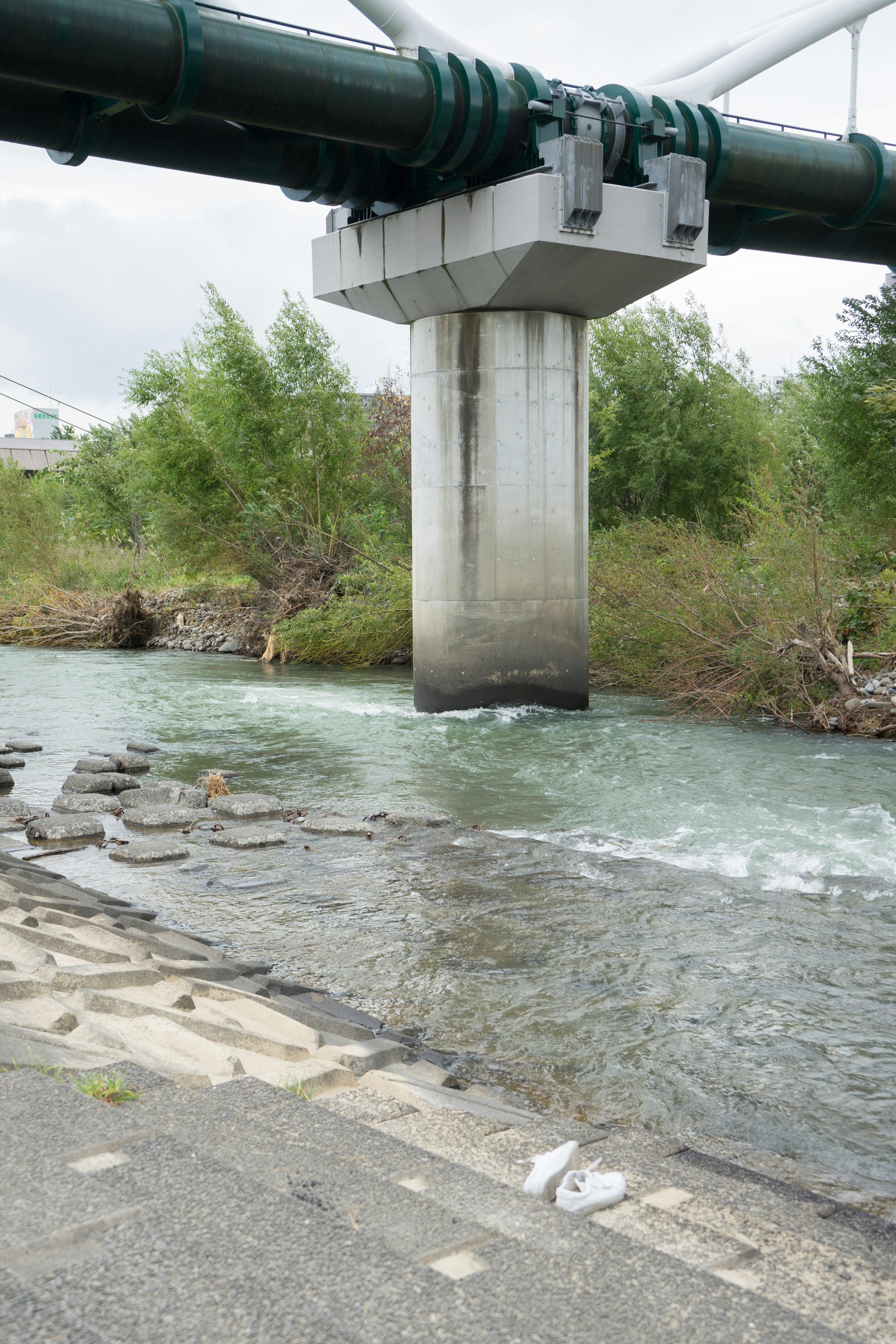 A bridge support pillar next to a river featuring green foliage and flowing water