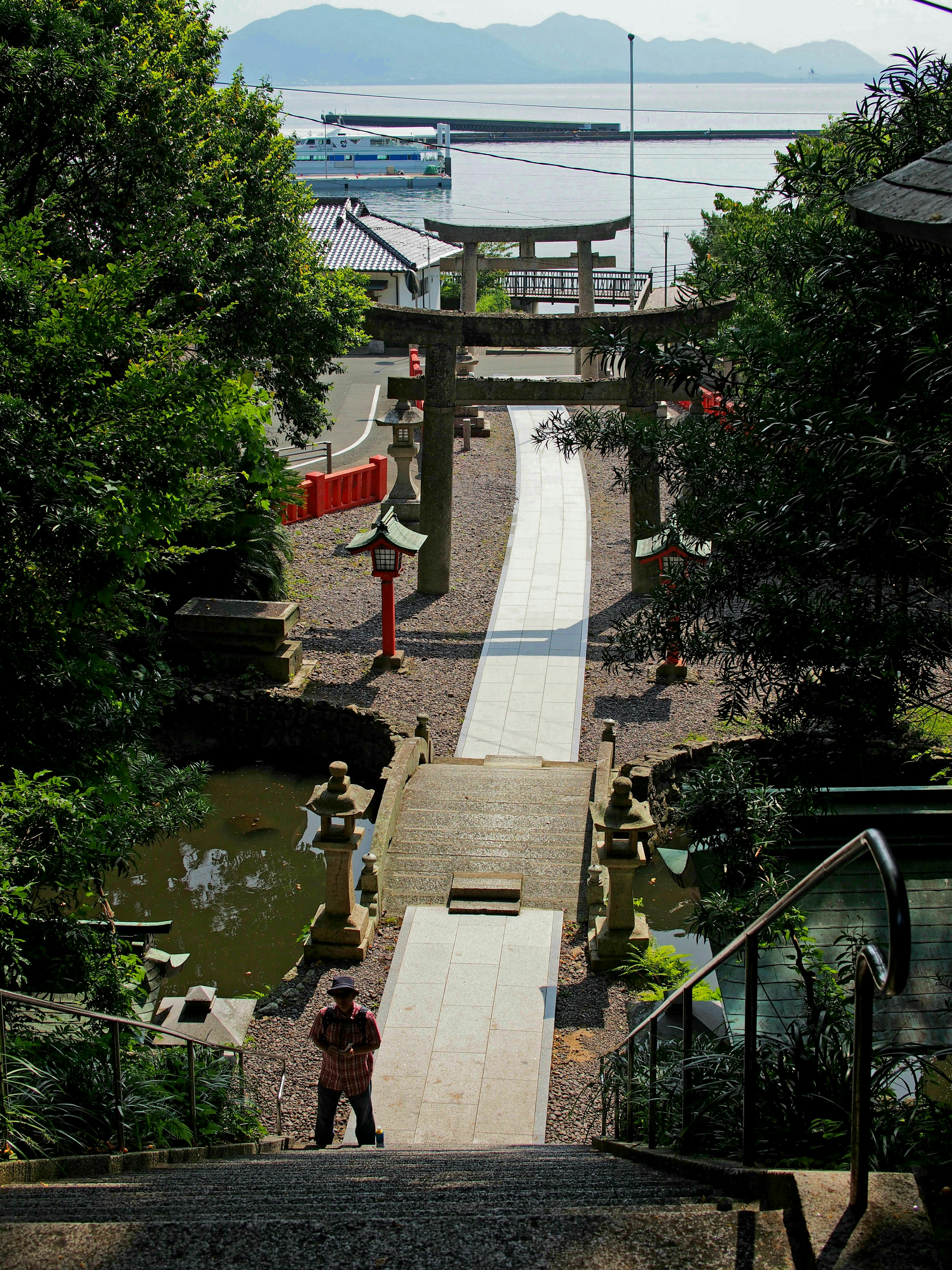 Scenic view of a shrine surrounded by greenery with a stone bridge and red torii gates