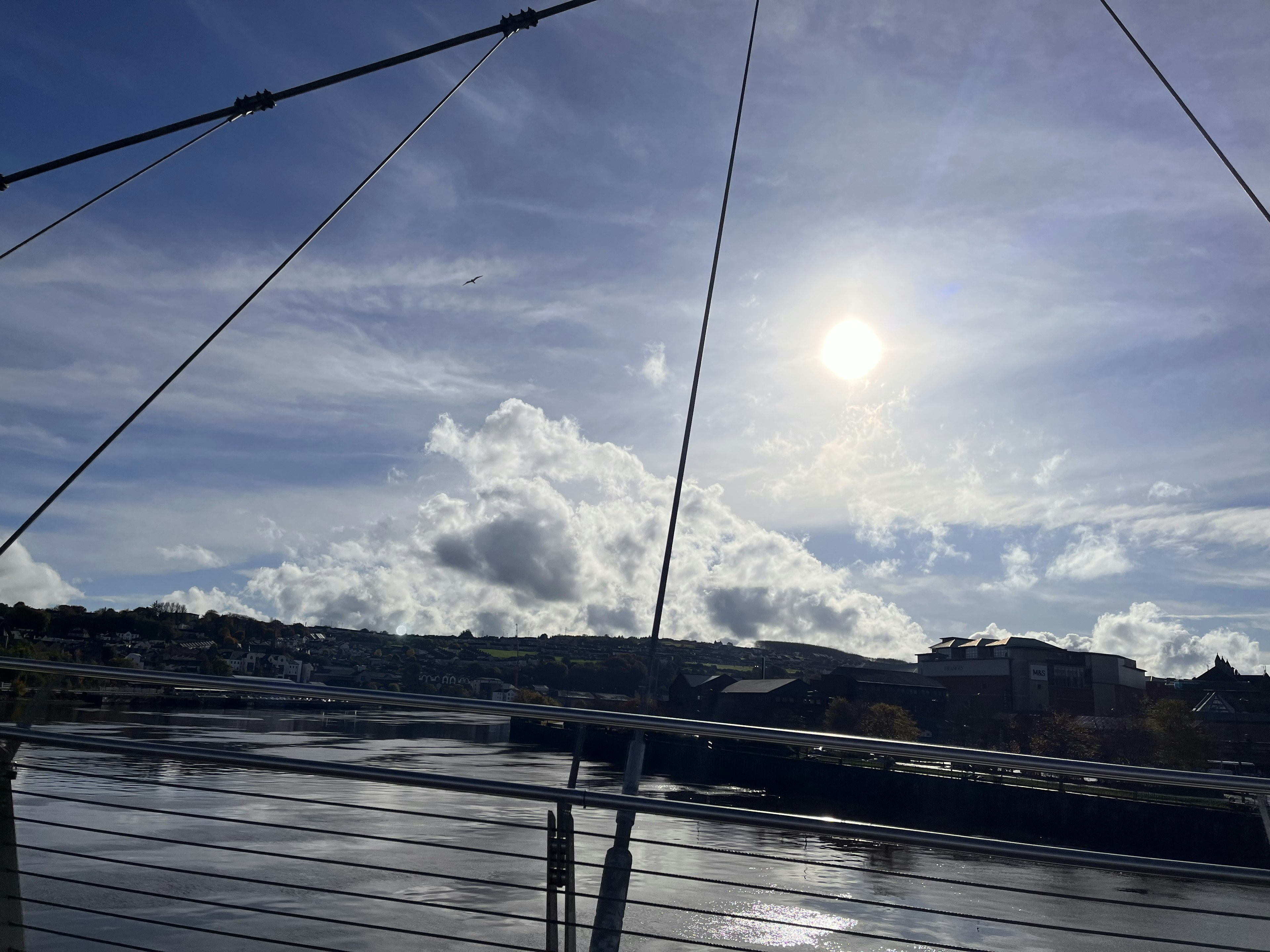 Una vista del río con cielo azul y nubes Cables del puente visibles Sol brillante