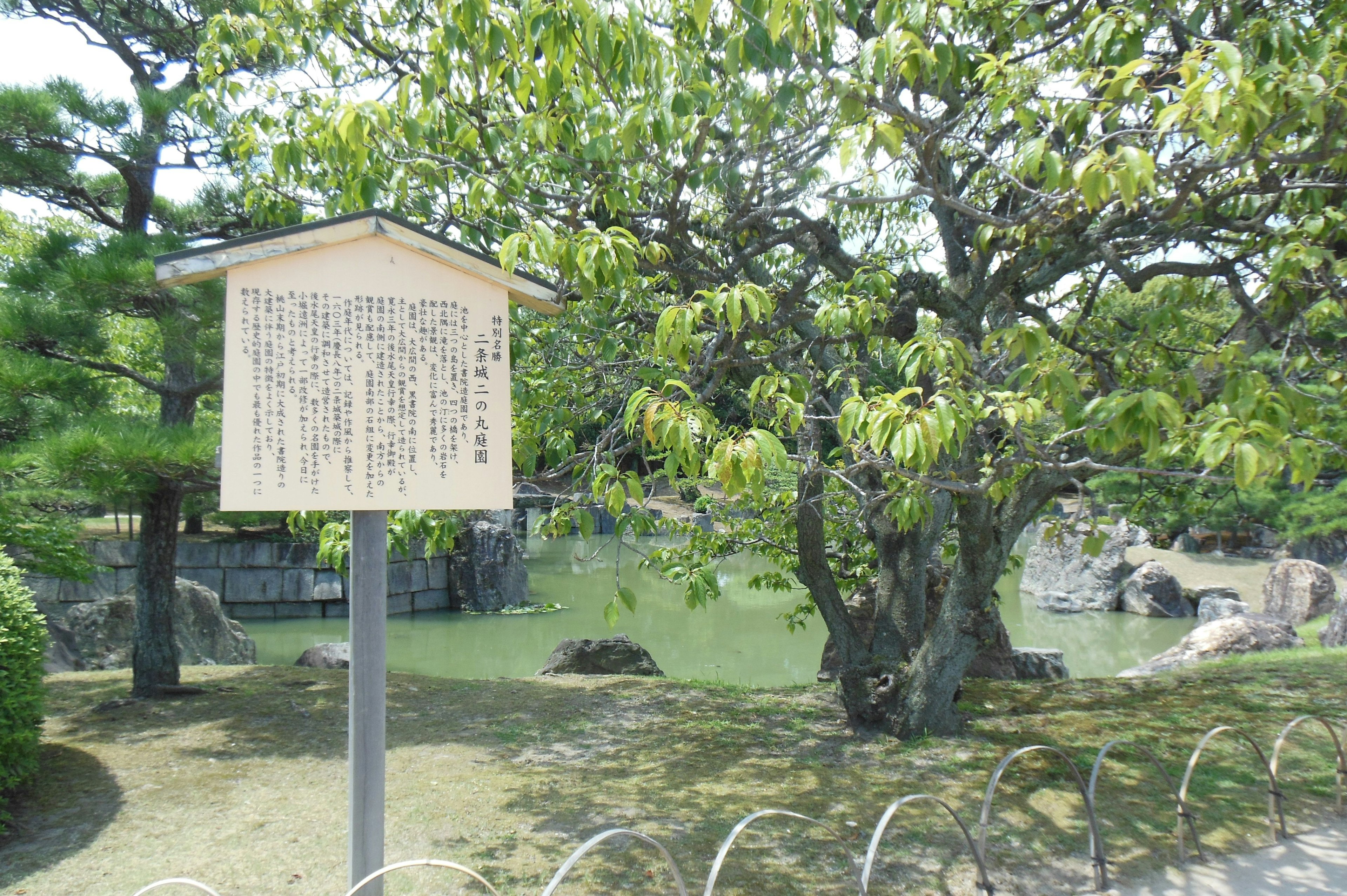 Papan informasi dekat kolam dengan pohon hijau subur