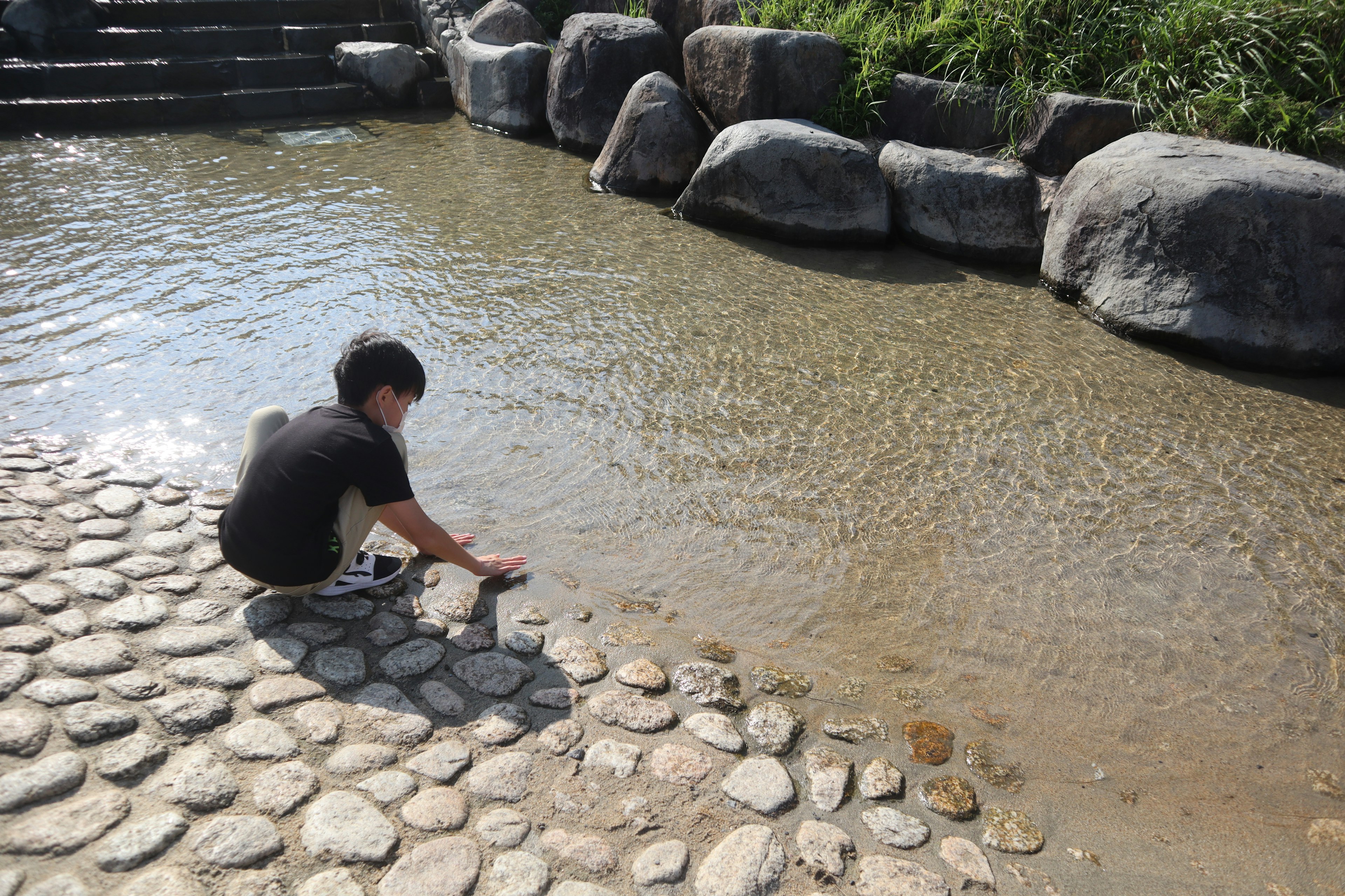 A child playing with water at a rocky riverbank