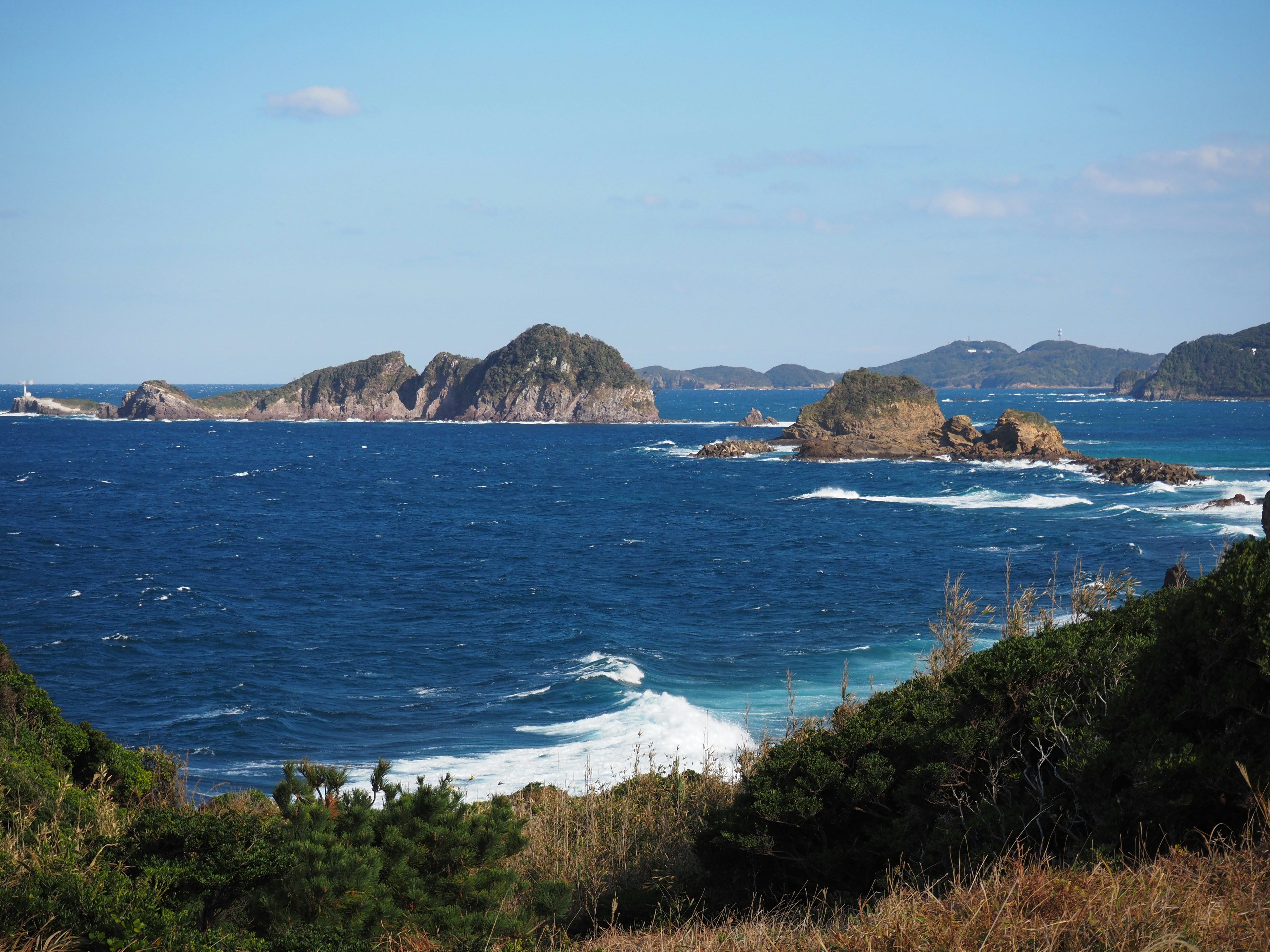 Scenic view of blue ocean with small islands and green grass in the foreground