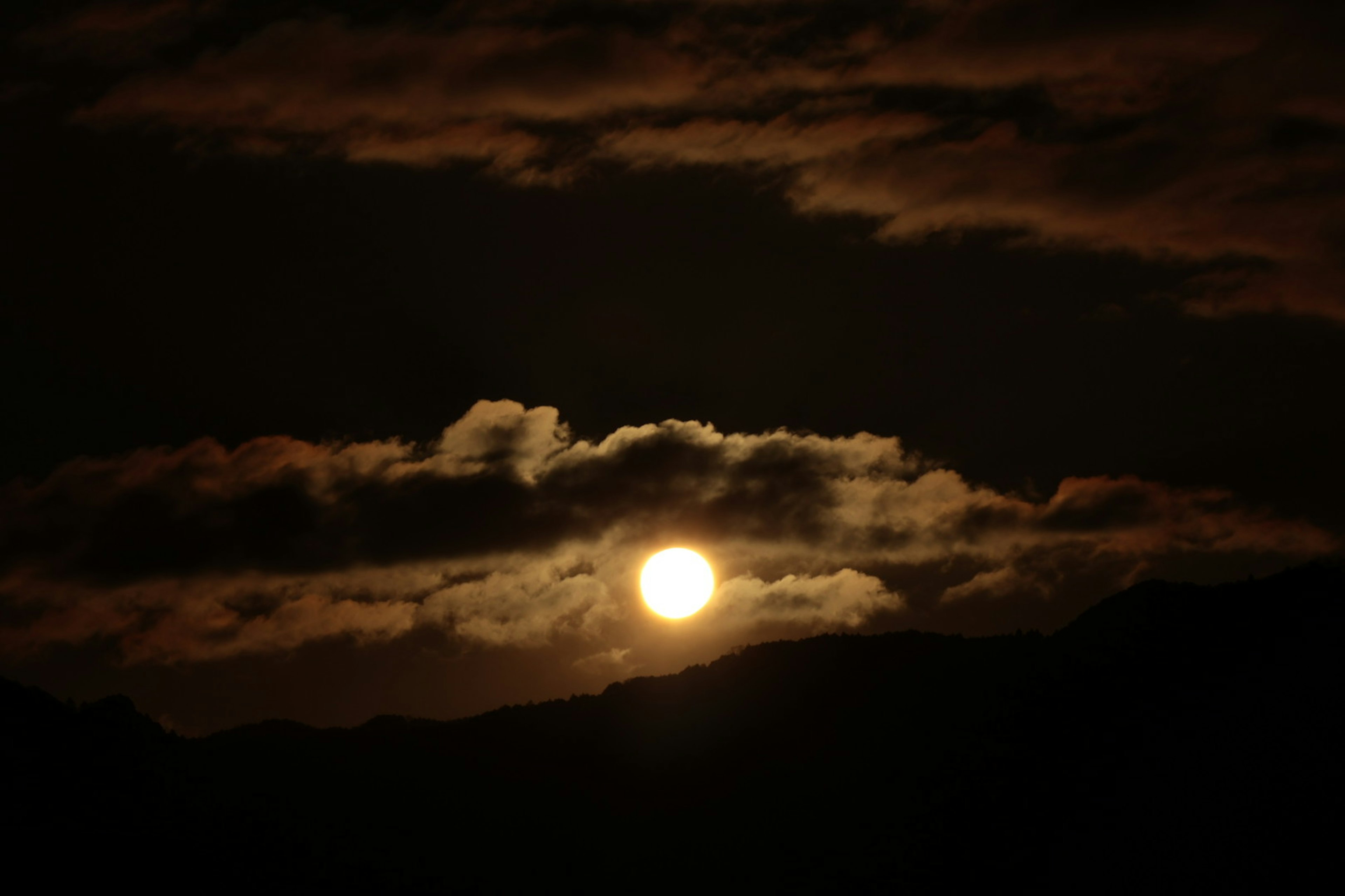 Sole che tramonta dietro nuvole scure con silhouette di montagna