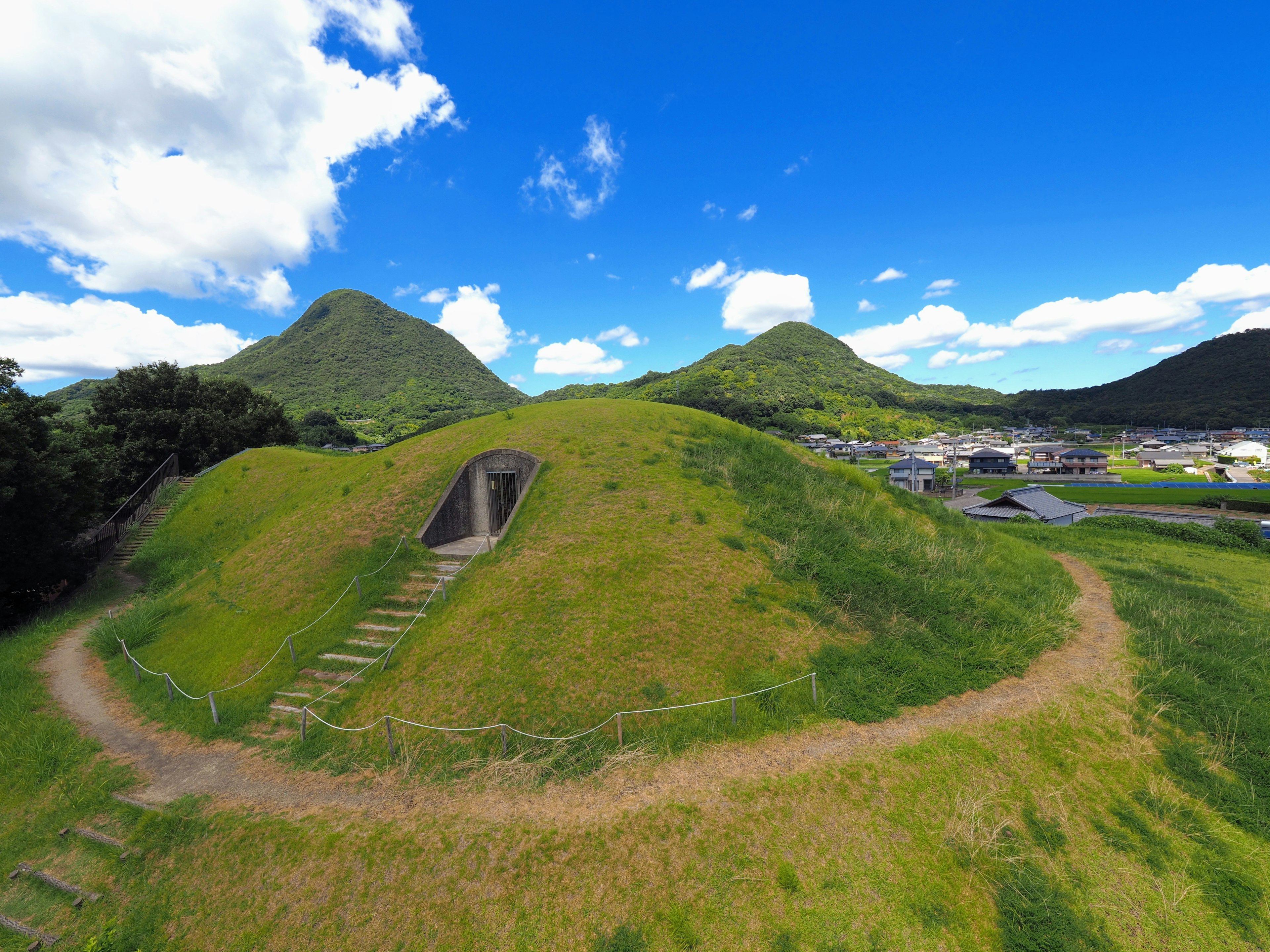 緑の丘と青い空の下にある古代の墳墓と周囲の風景