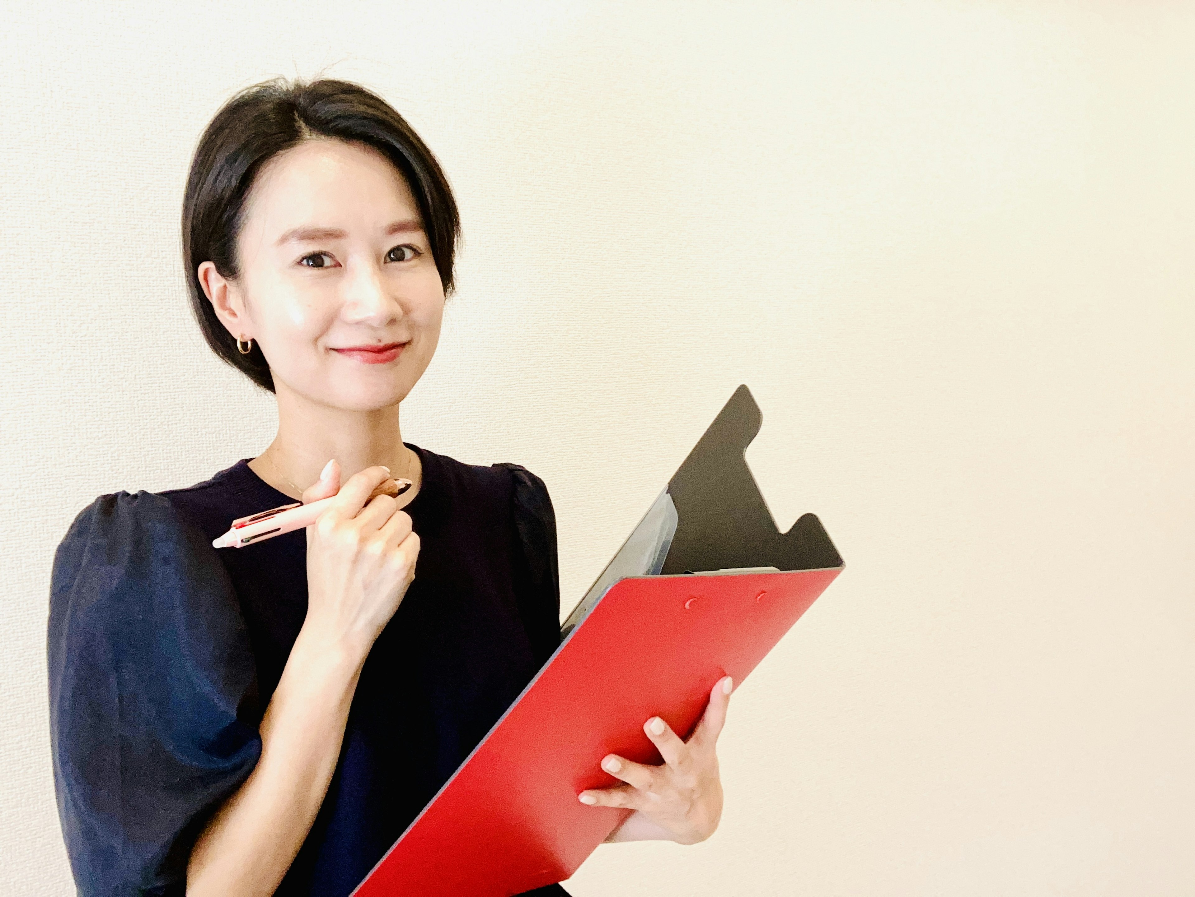 Donna in blusa nera che tiene un clipboard rosso e una penna con un'espressione pensierosa