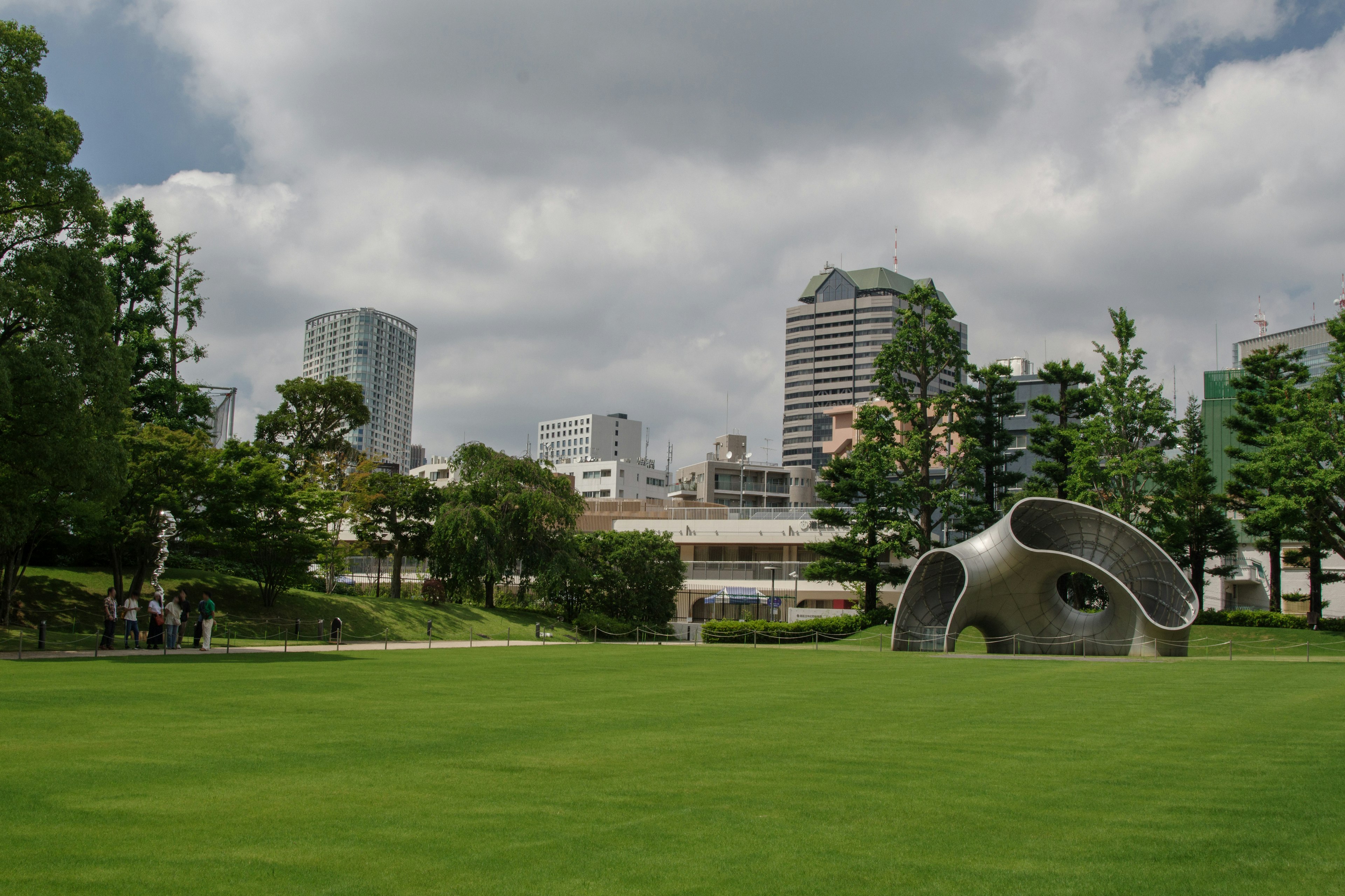 公園裡寬廣的綠草坪上有現代雕塑，背景是城市天際線