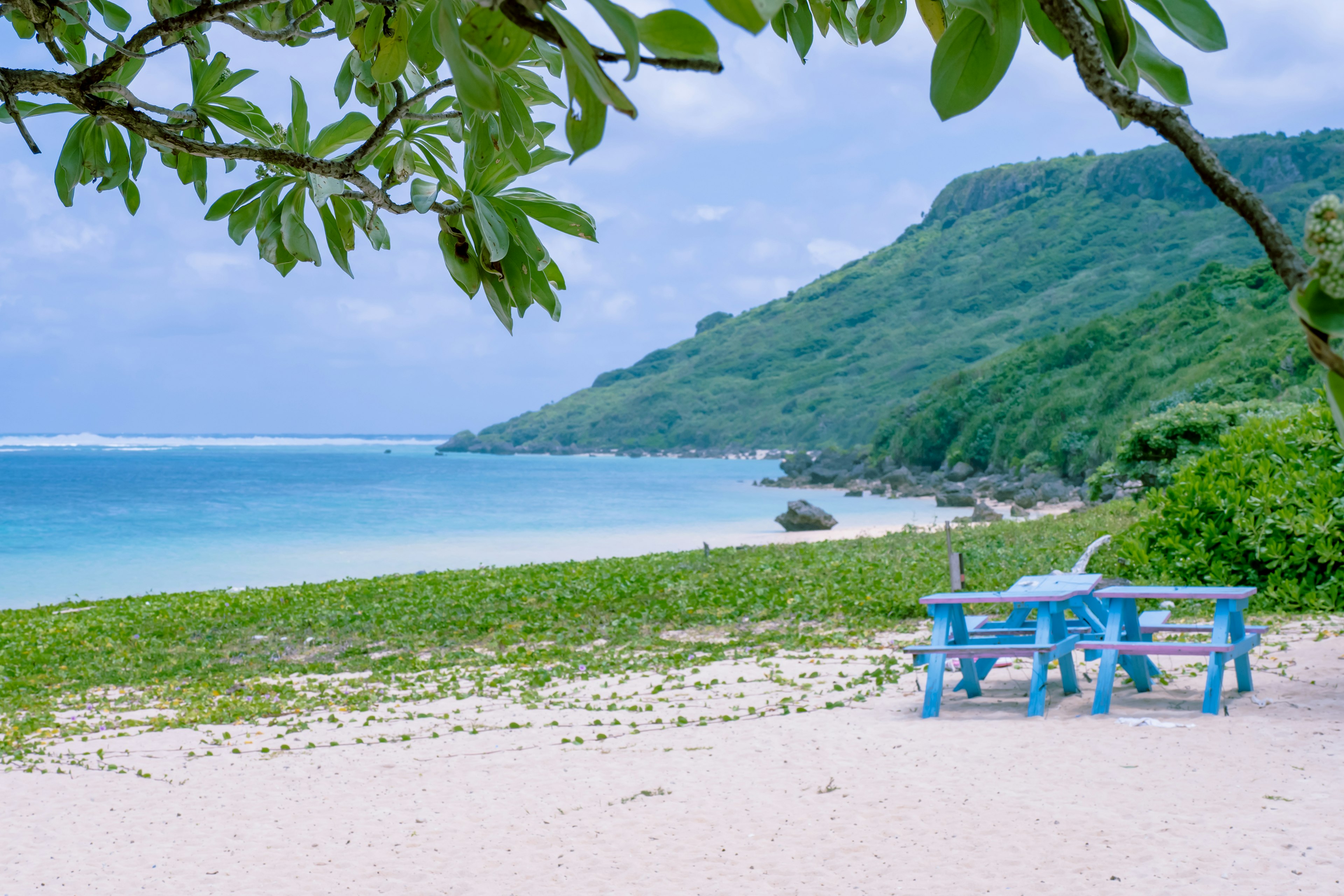 Pemandangan pantai yang indah dengan meja dan kursi piknik biru perbukitan hijau dan laut tenang