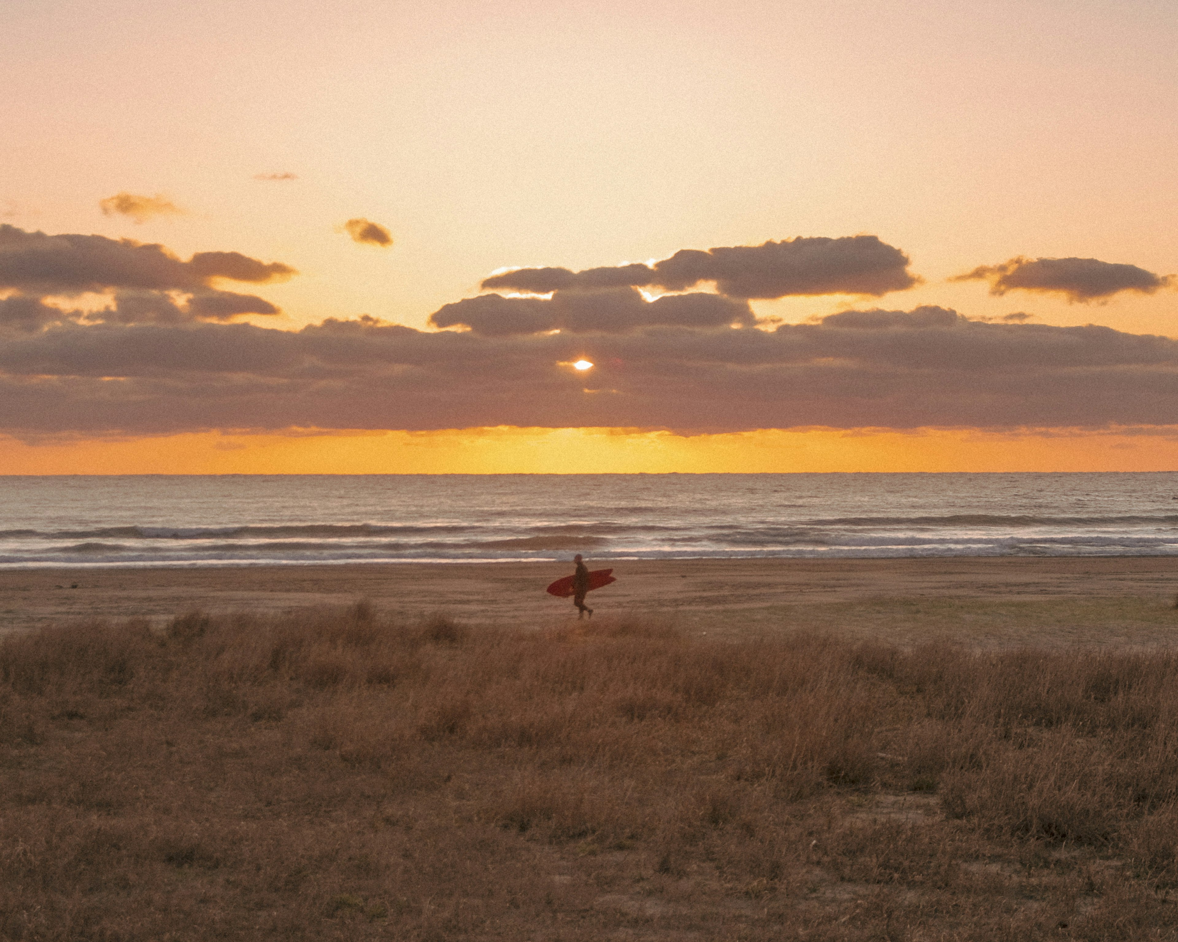 Surfer mit einem Surfbrett am Strand während eines wunderschönen Sonnenuntergangs