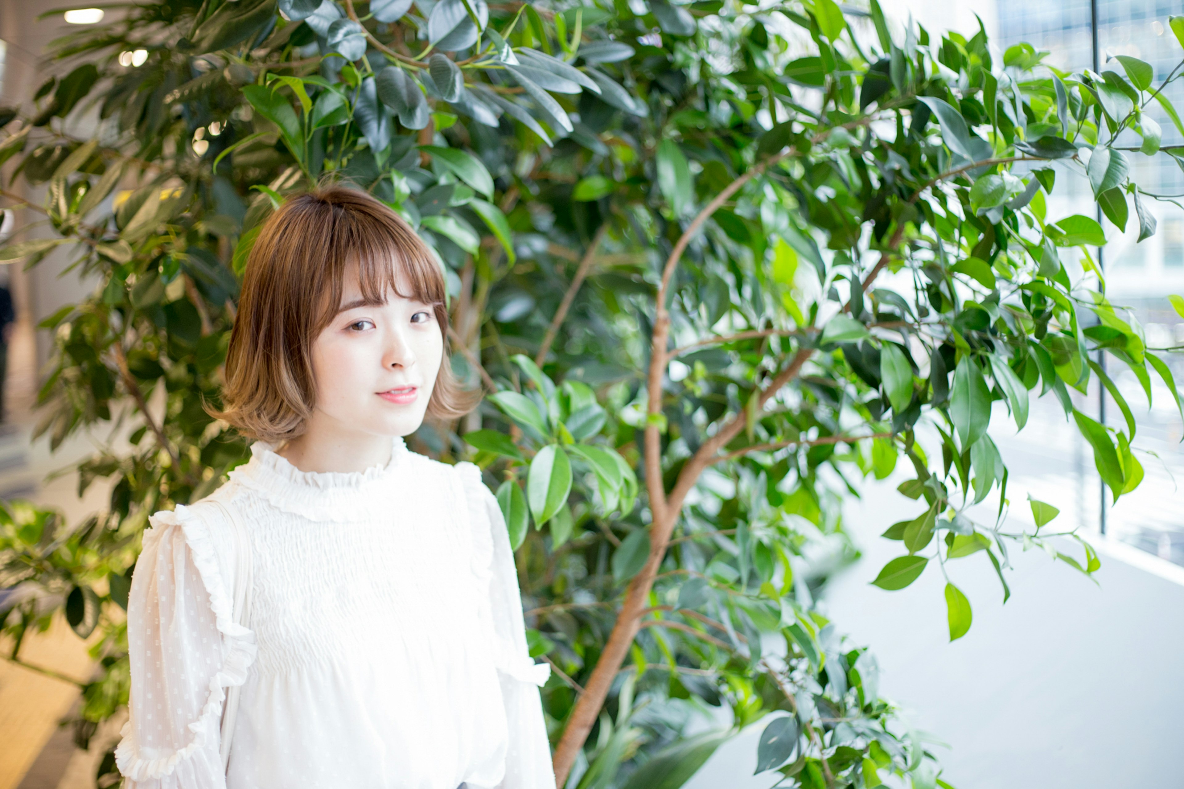 Portrait d'une femme devant des plantes vertes portant un chemisier blanc