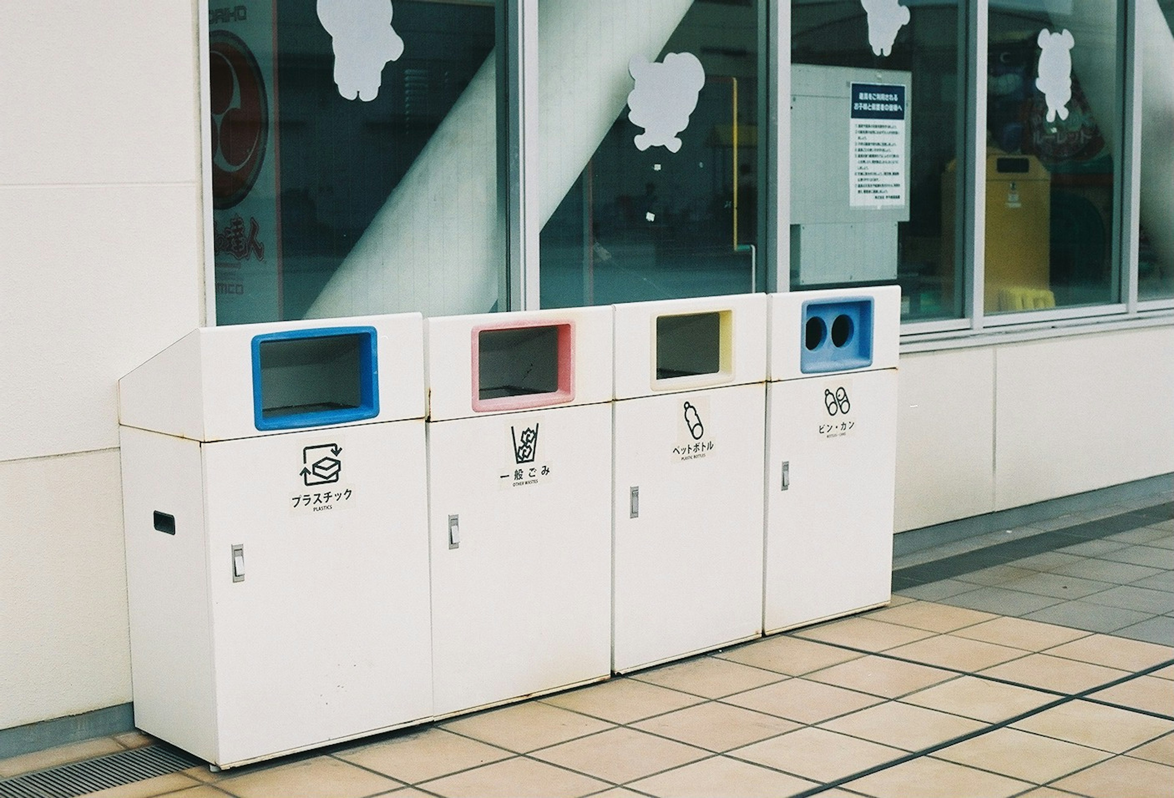 Cuatro contenedores de reciclaje blancos alineados frente a una pared que promueve la conciencia ambiental