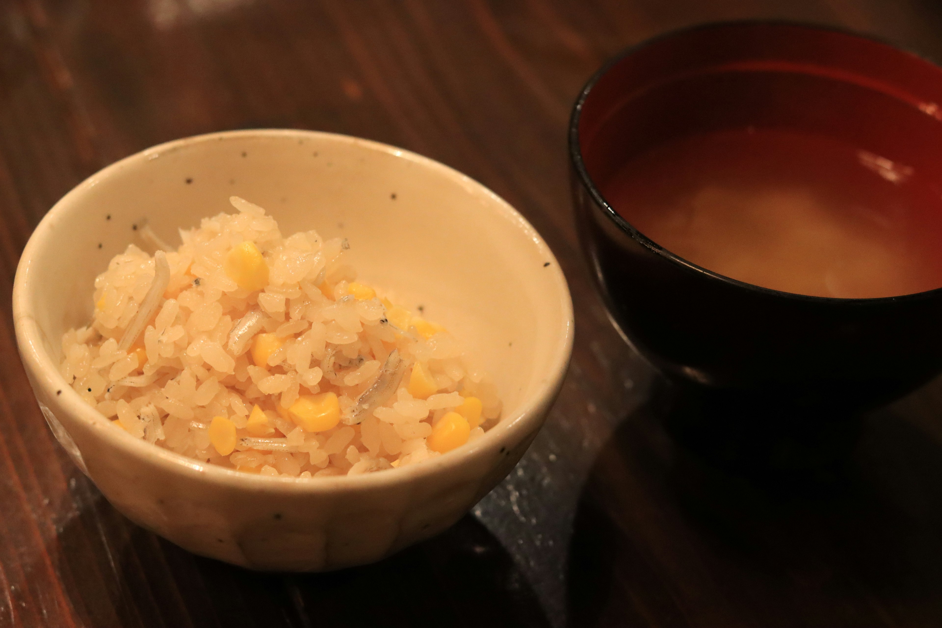 Schüssel Reis mit Mais und eine Tasse Miso-Suppe auf einem Holztisch