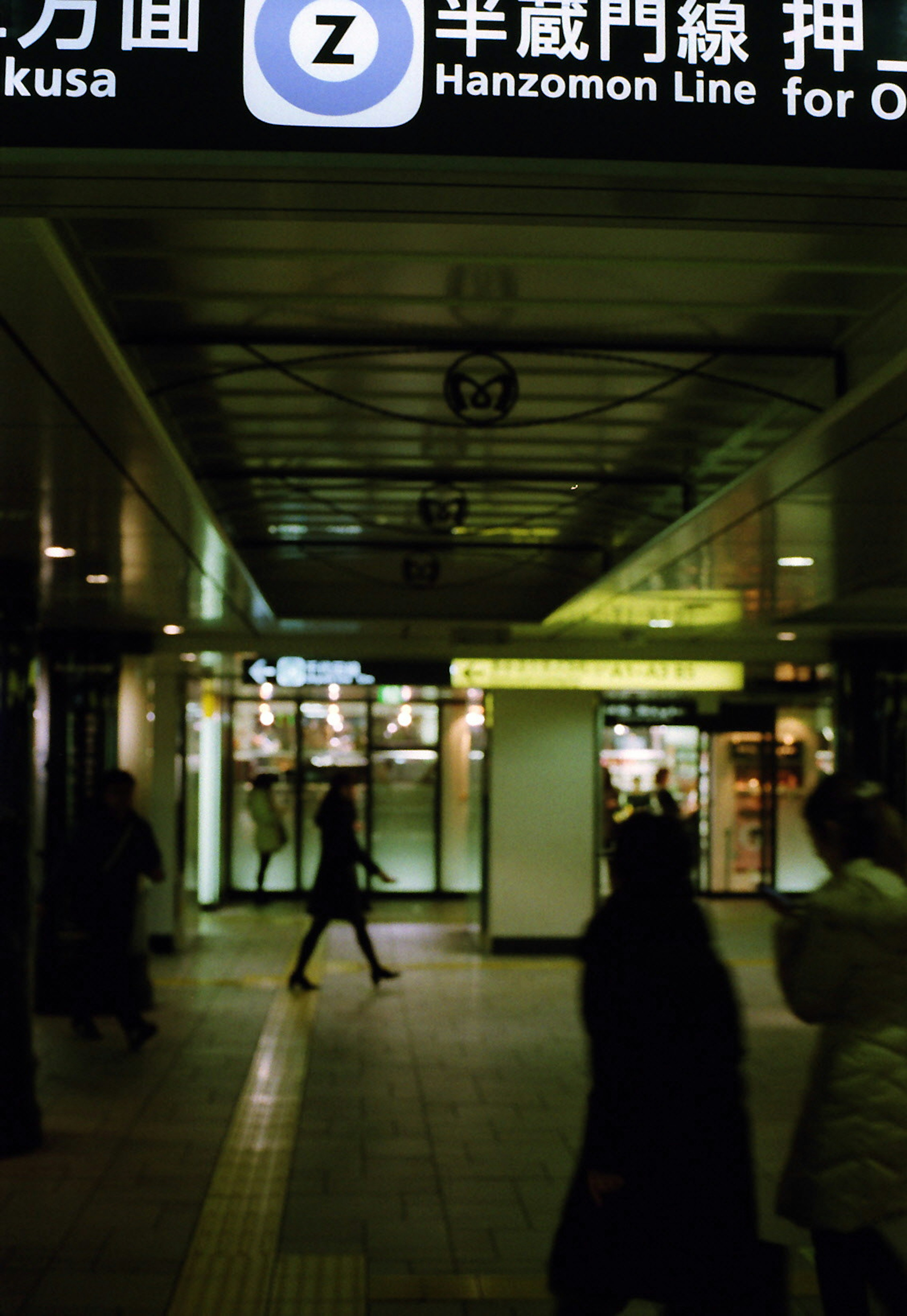 Couloir de métro faiblement éclairé avec des personnes marchant et des panneaux en japonais