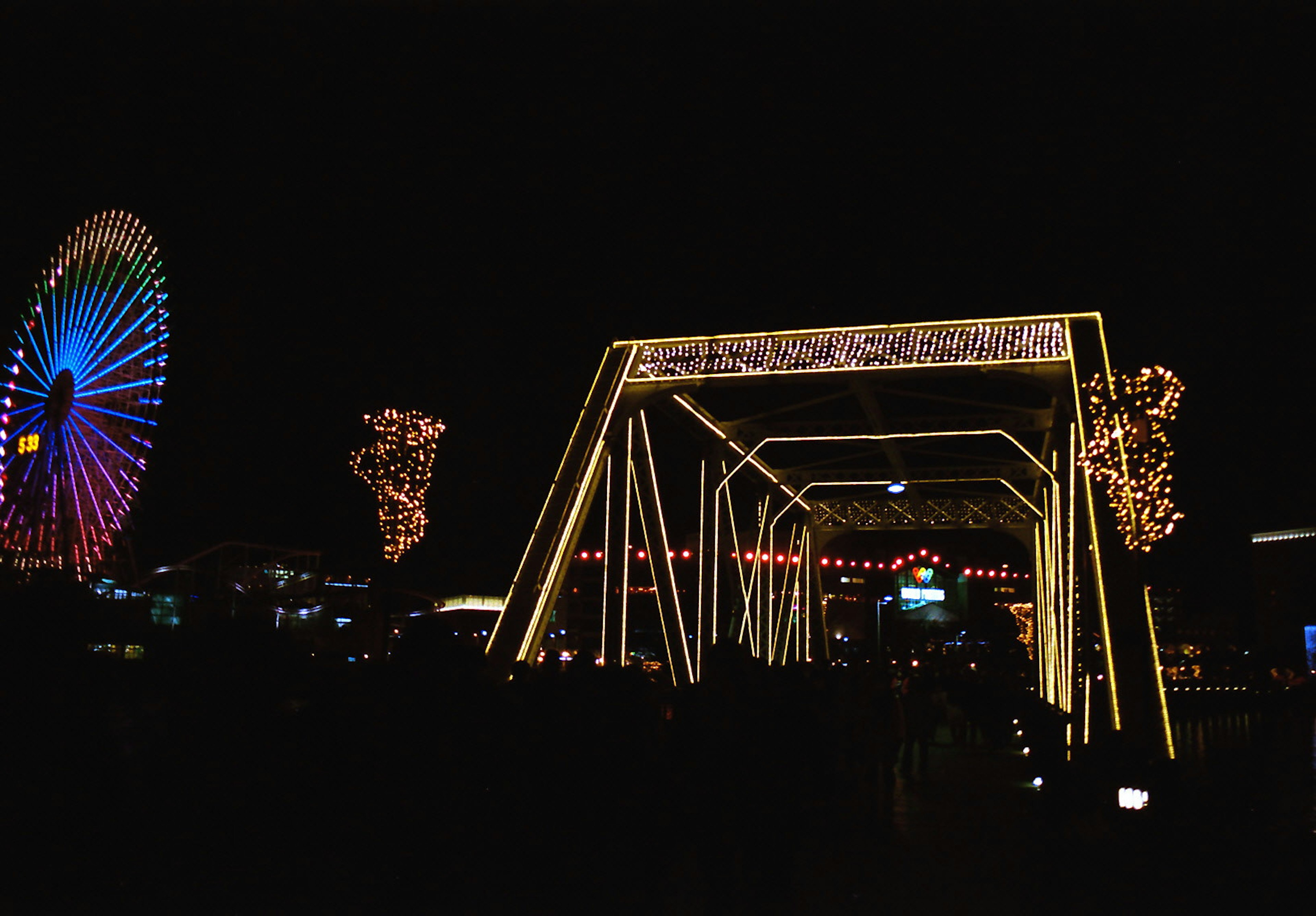 Rueda de la fortuna colorida y puente iluminado en un parque de atracciones nocturno