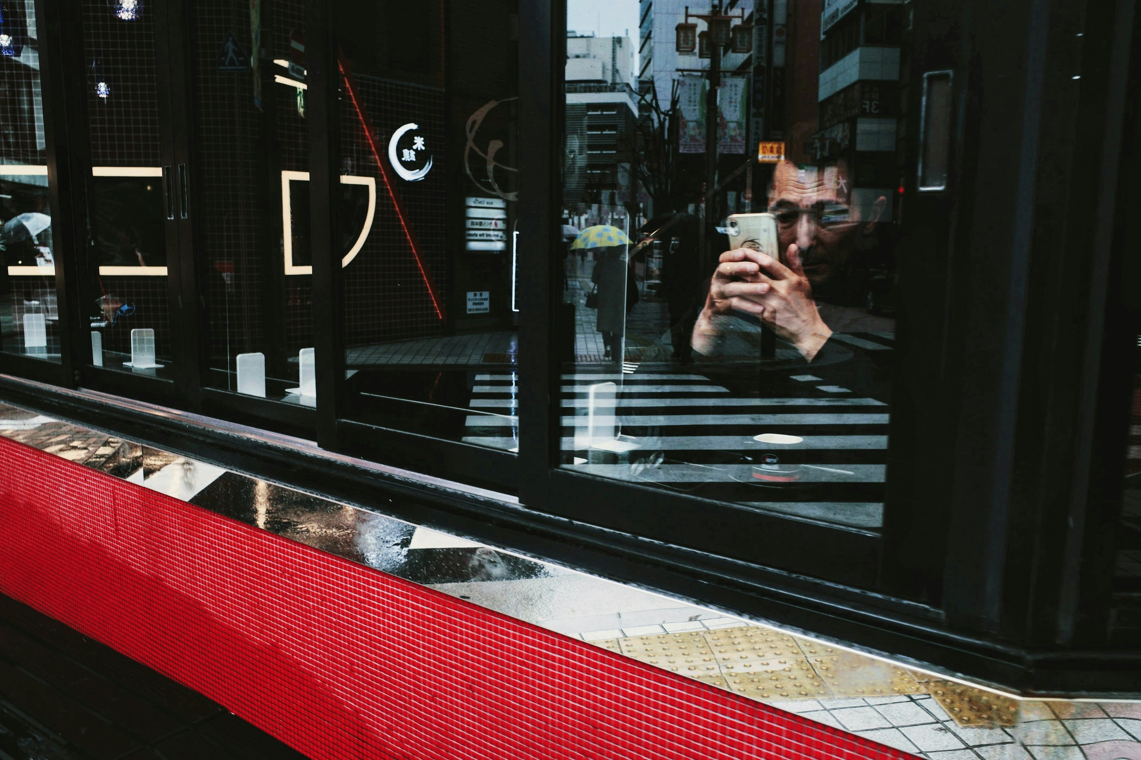 Ein Mann mit einem Smartphone, der in einem Fenster in einer städtischen Umgebung reflektiert wird