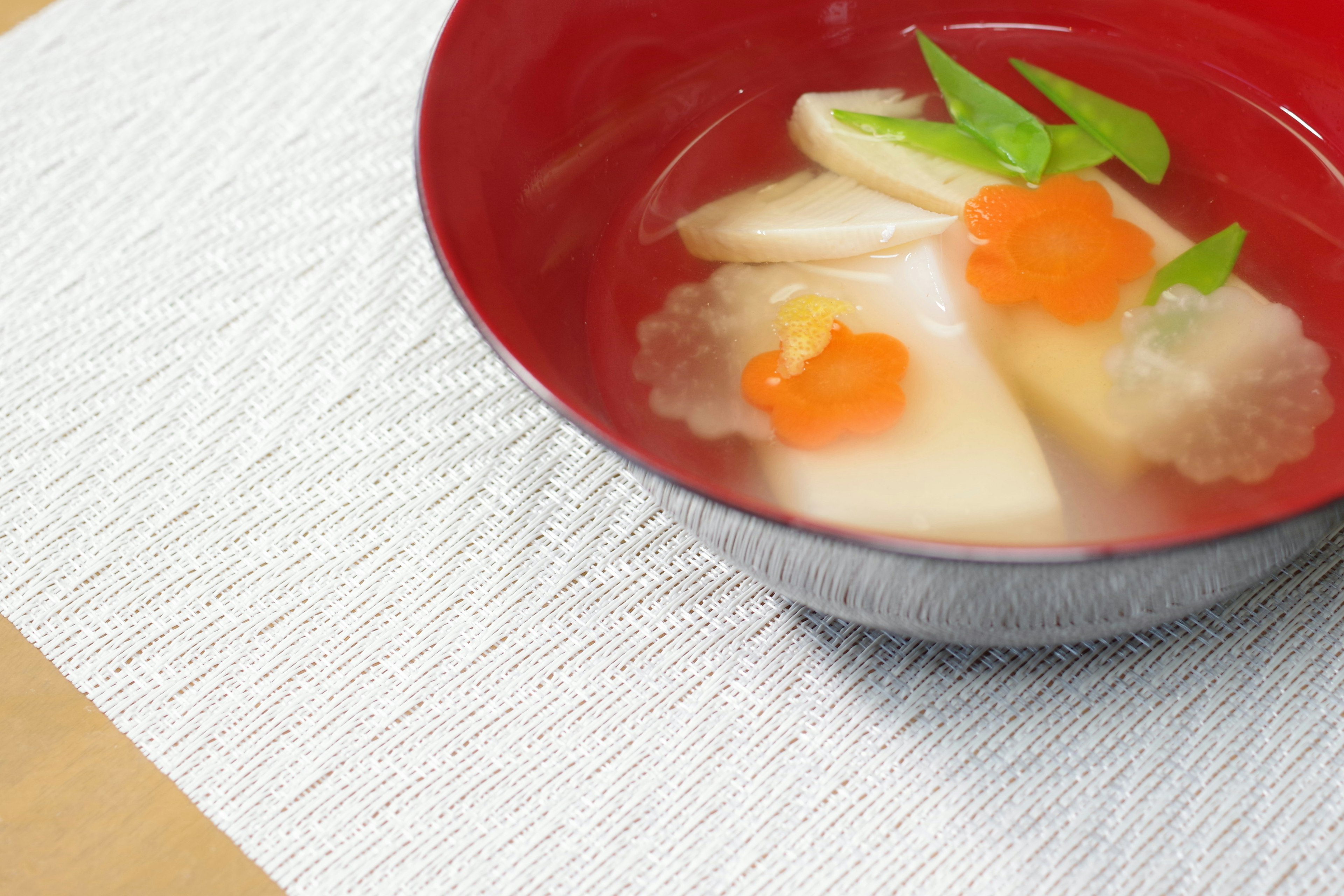 Soupe claire dans un bol rouge avec des légumes et des garnitures