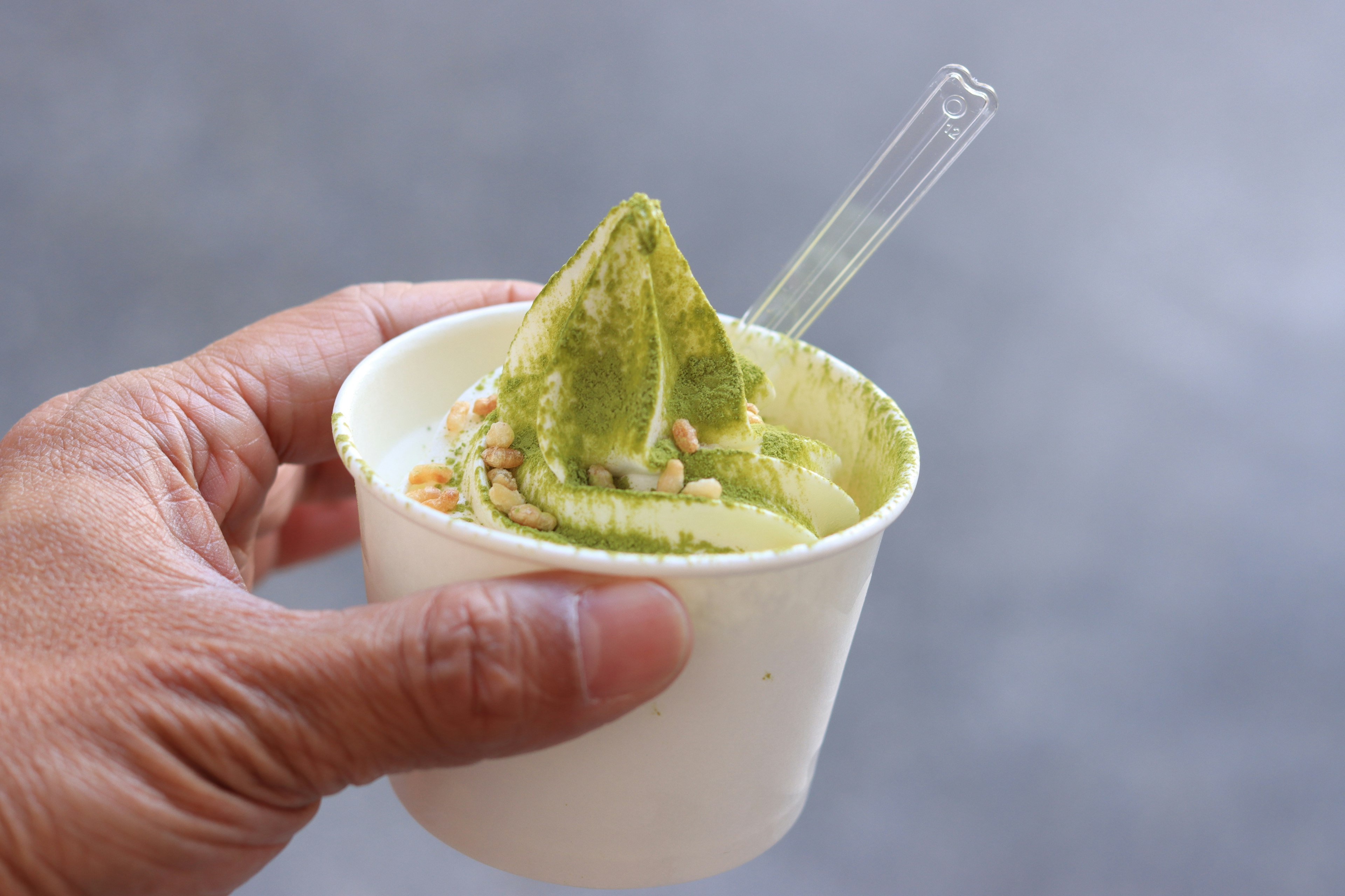 A hand holding a cup of green dessert with a spoon