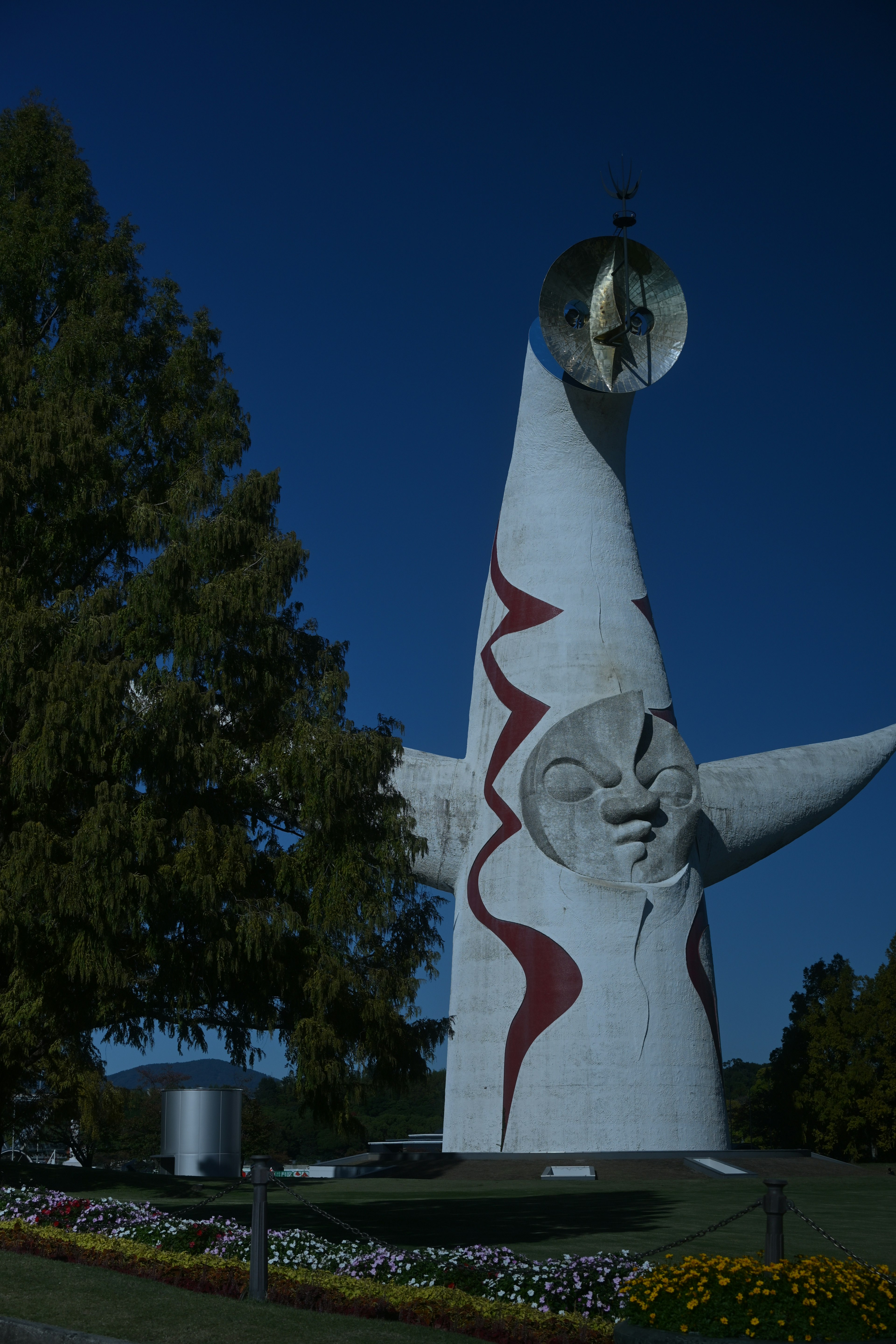 Una alta escultura blanca con patrones rojos y una cara bajo un cielo azul