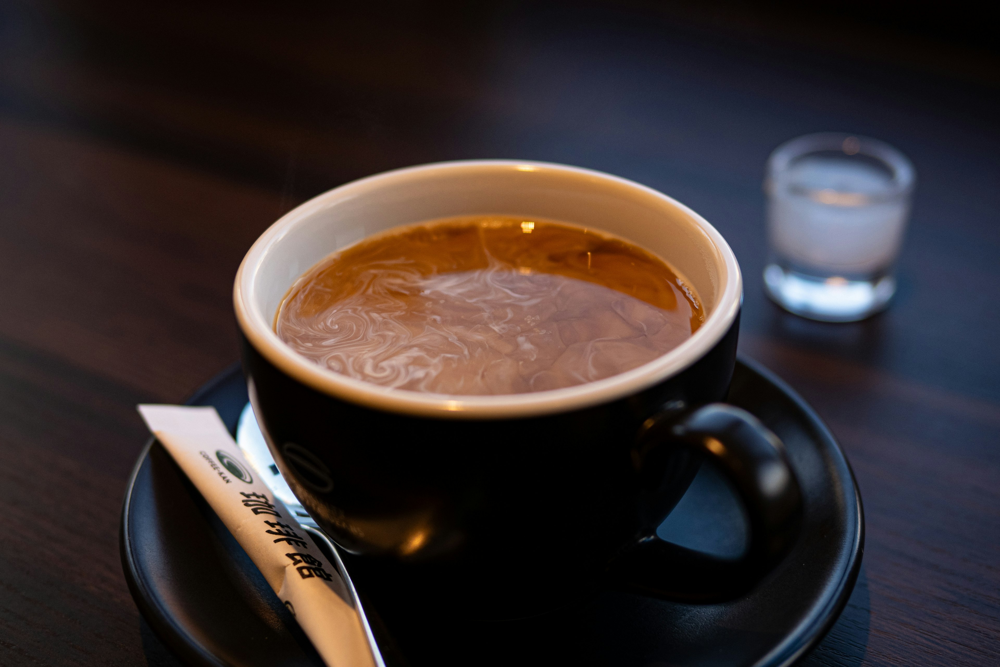 Café caliente en una taza negra con un pequeño vaso de agua