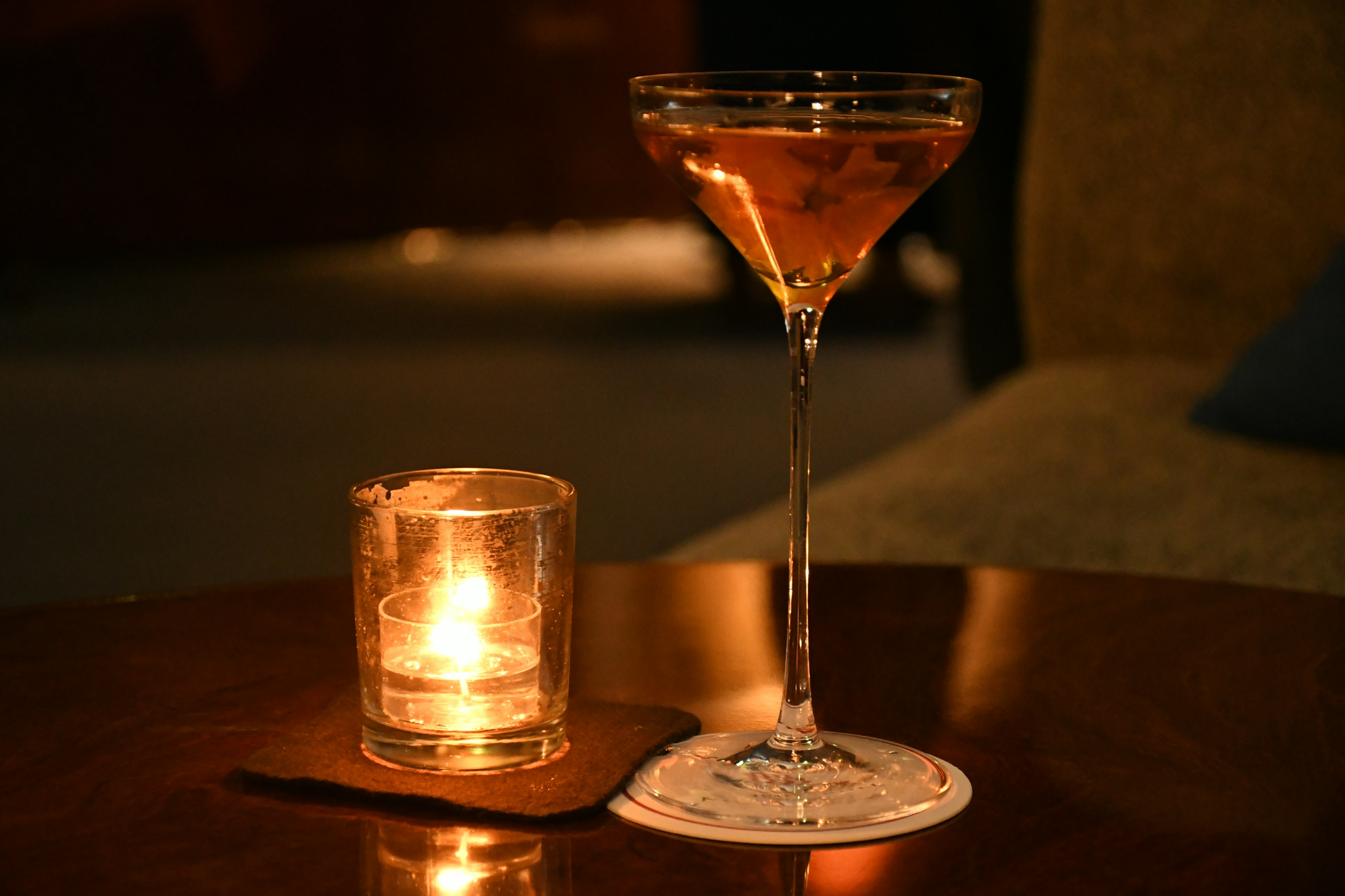 Verre à cocktail avec boisson ambrée et bougie lumineuse sur une table en bois