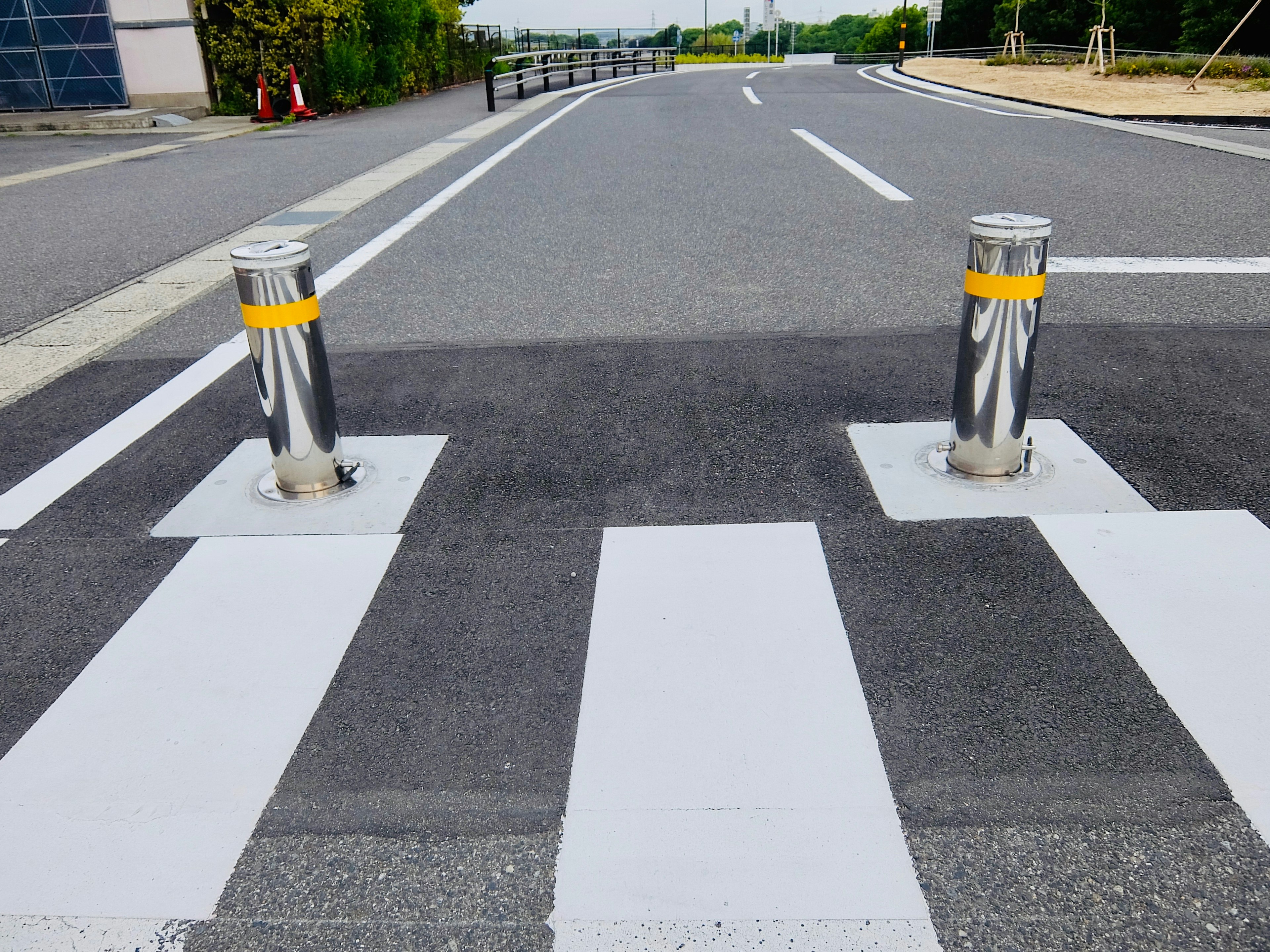 Dua bollard perak di jalan dengan zebra cross putih