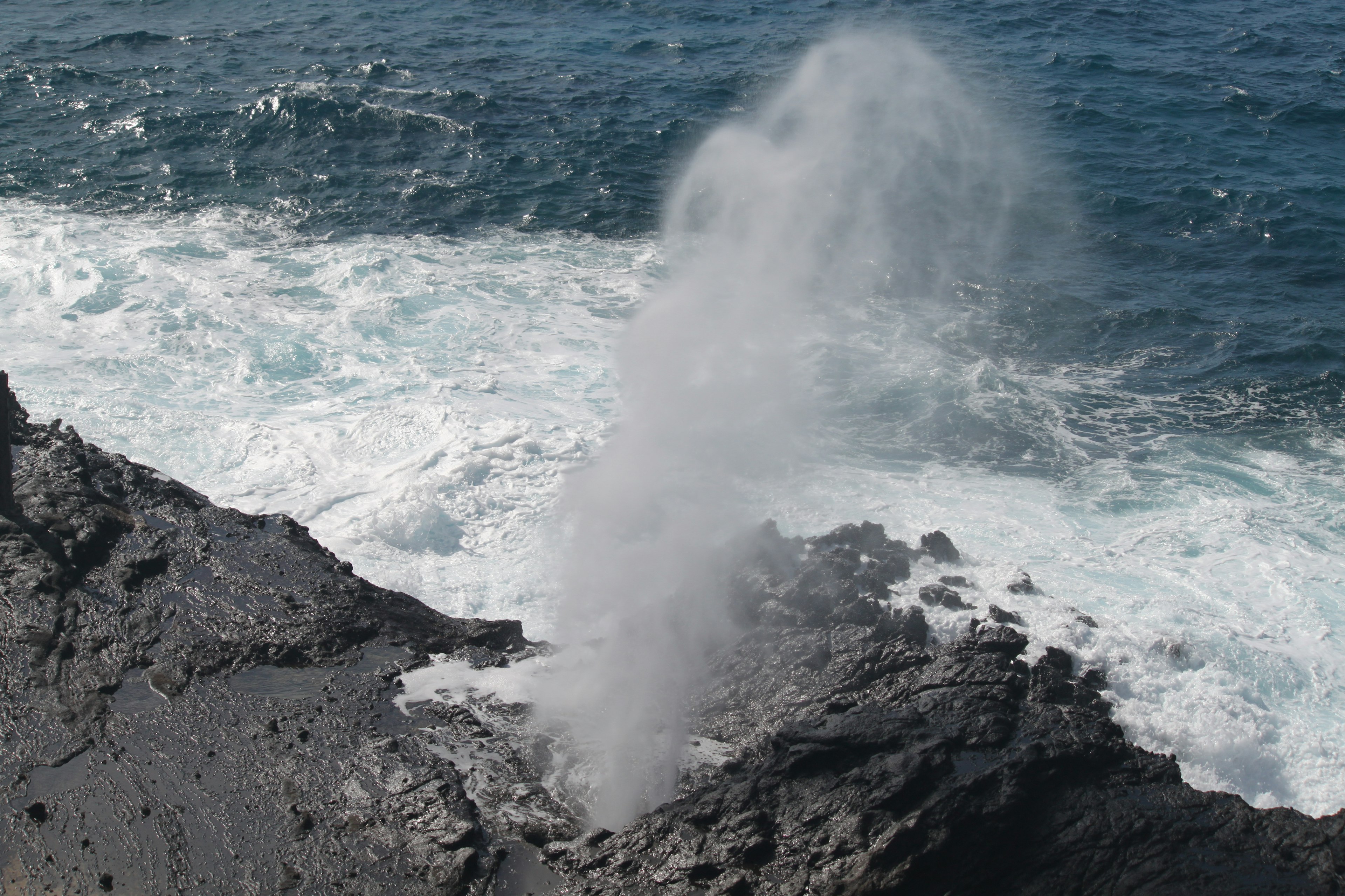 Water spouting from black rock into the ocean