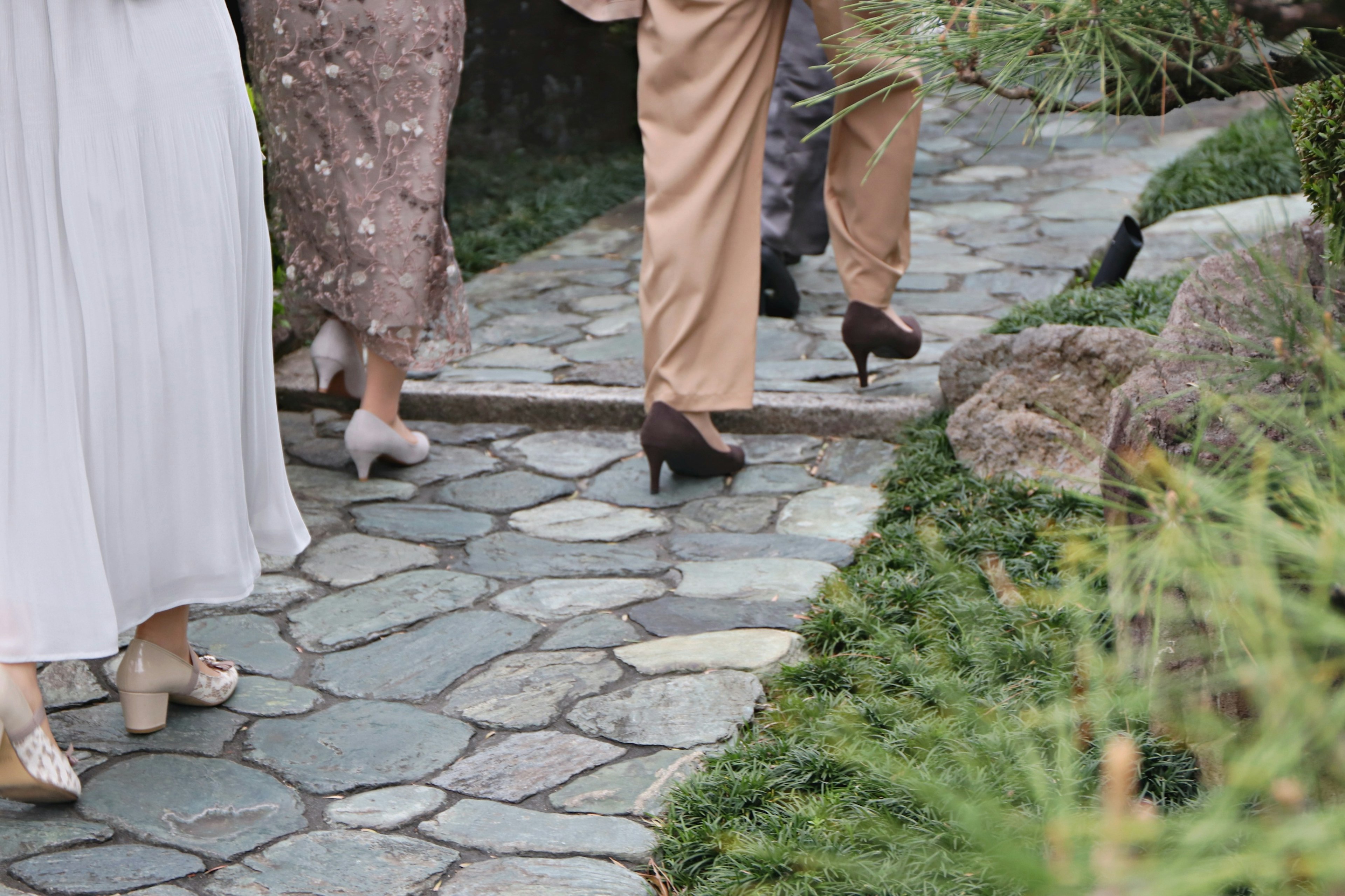 Personas caminando por un camino de piedra con calzado elegante y un entorno verde