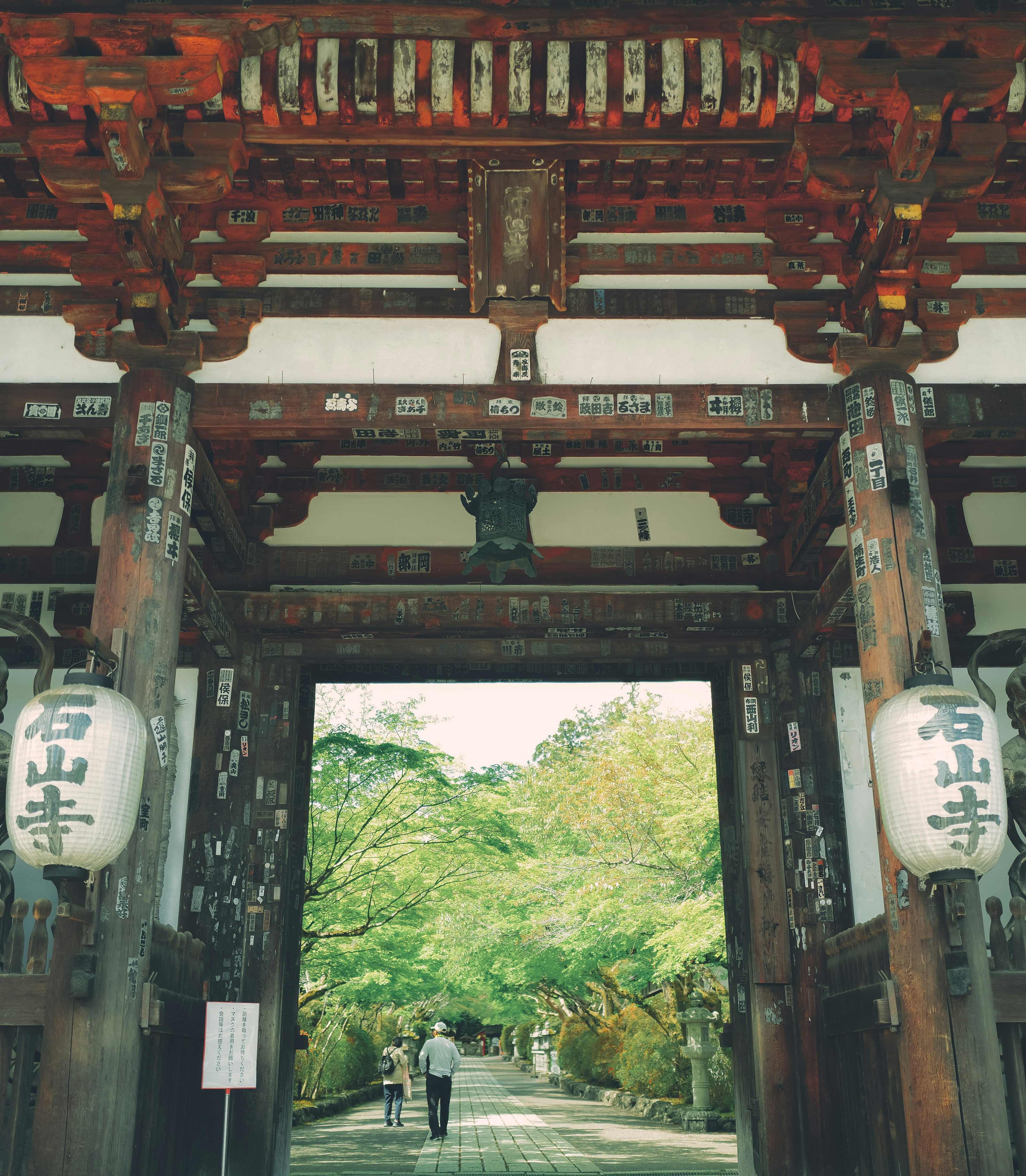 Entrada de un templo japonés tradicional con puerta de madera roja y jardín verde