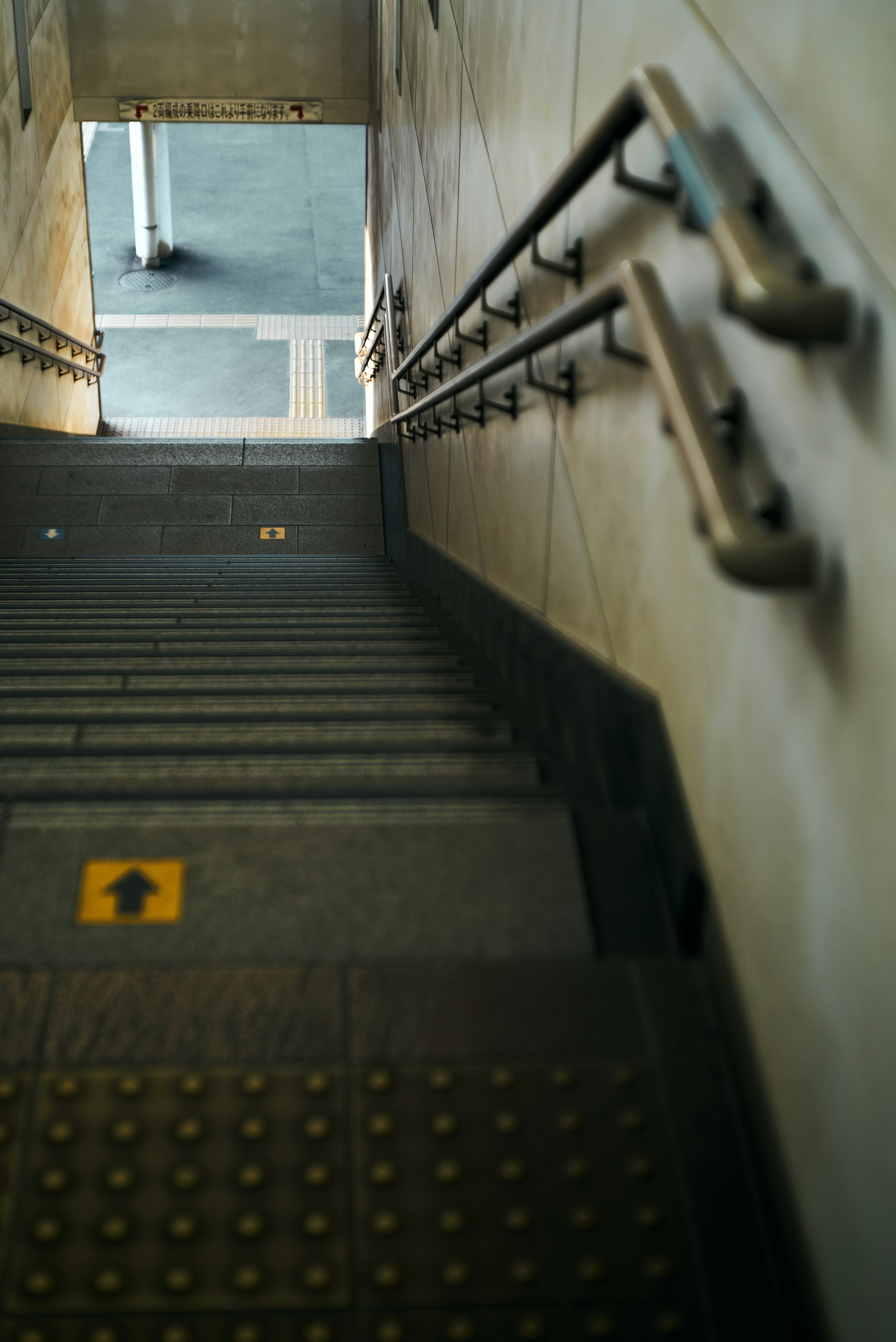 Blick nach unten auf eine Treppe mit Handläufen und einem gelben Pfeilschild