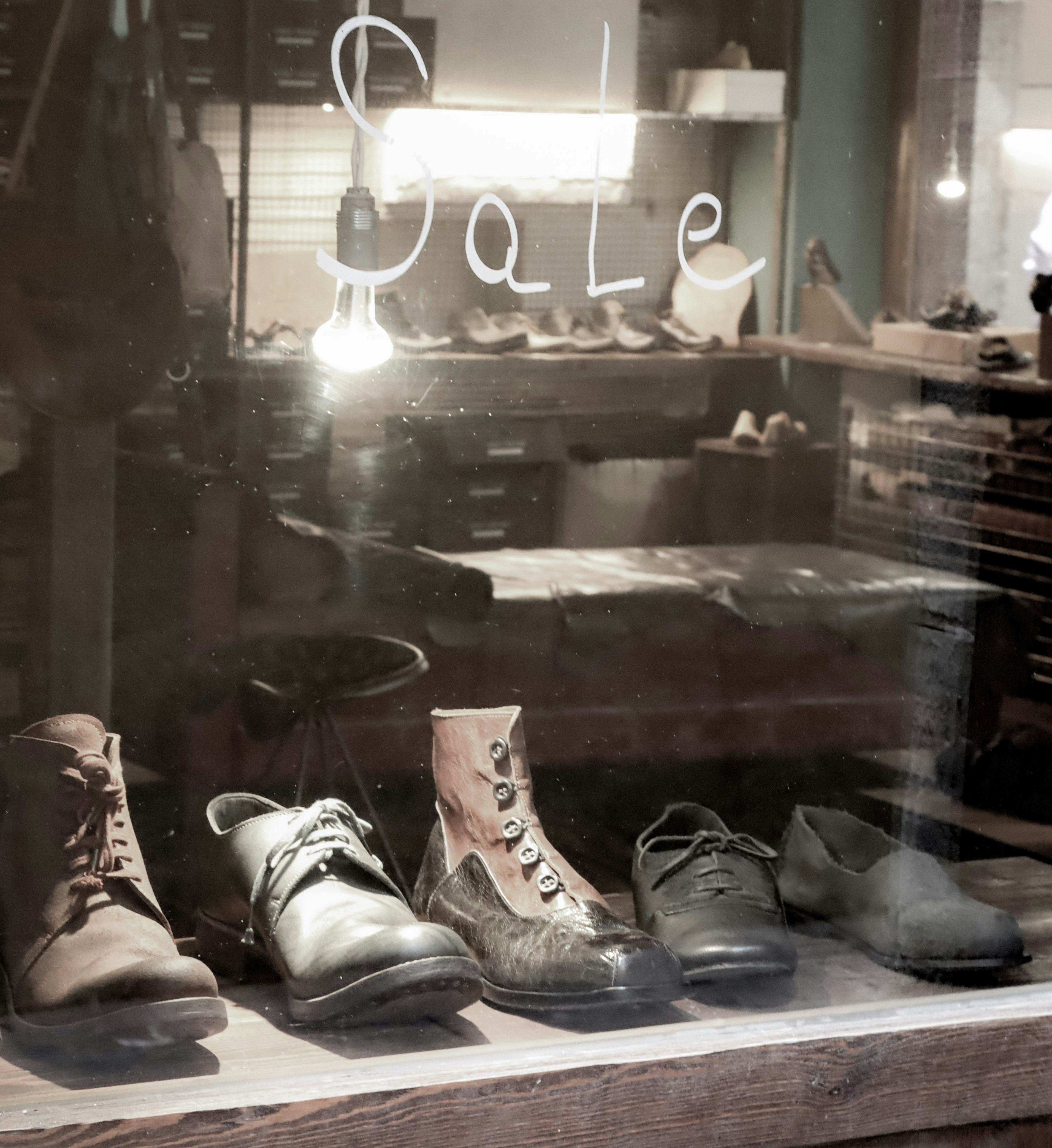 Various shoes displayed in a shop window with a sale sign