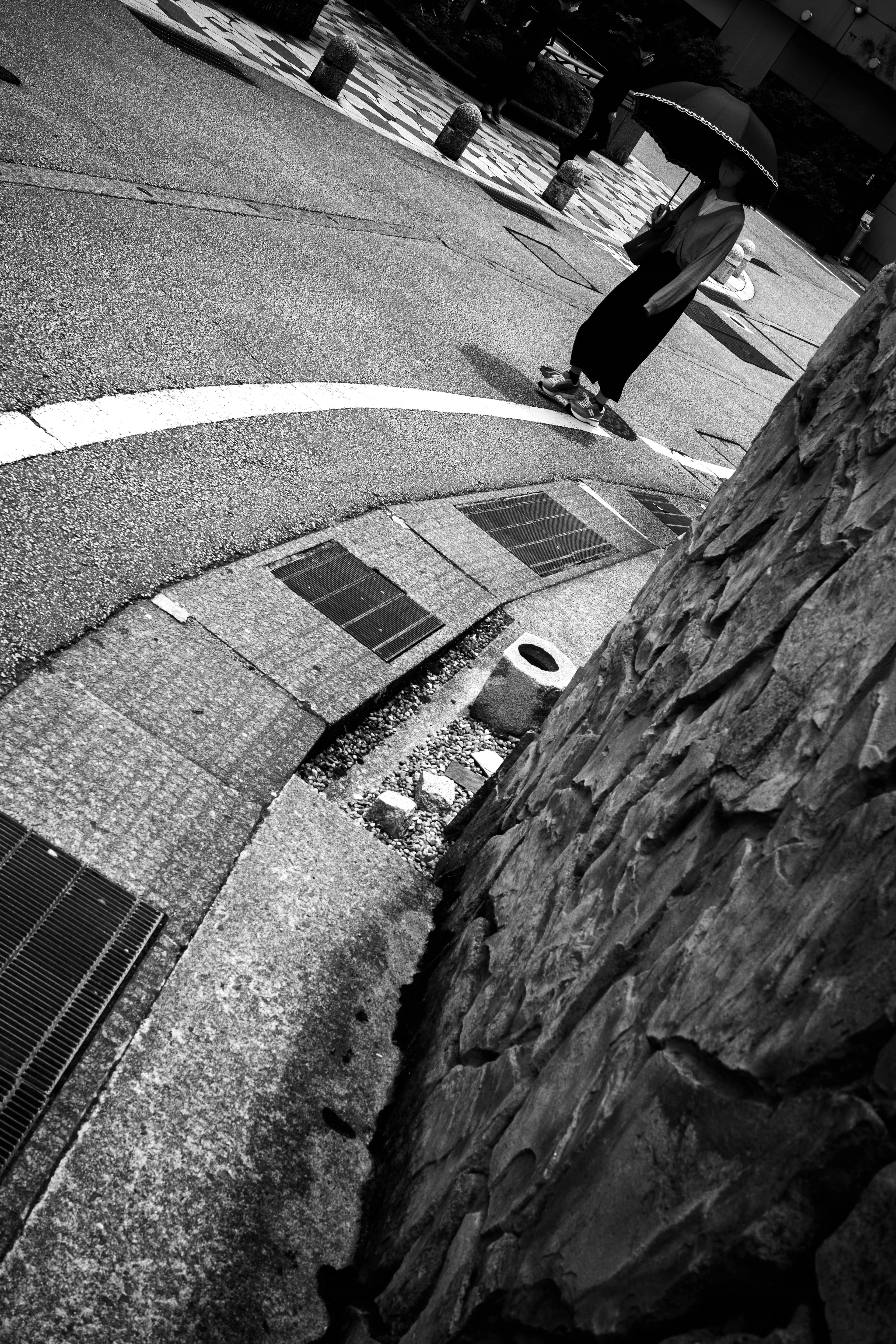 A person holding an umbrella stands at a street corner in a black and white scene