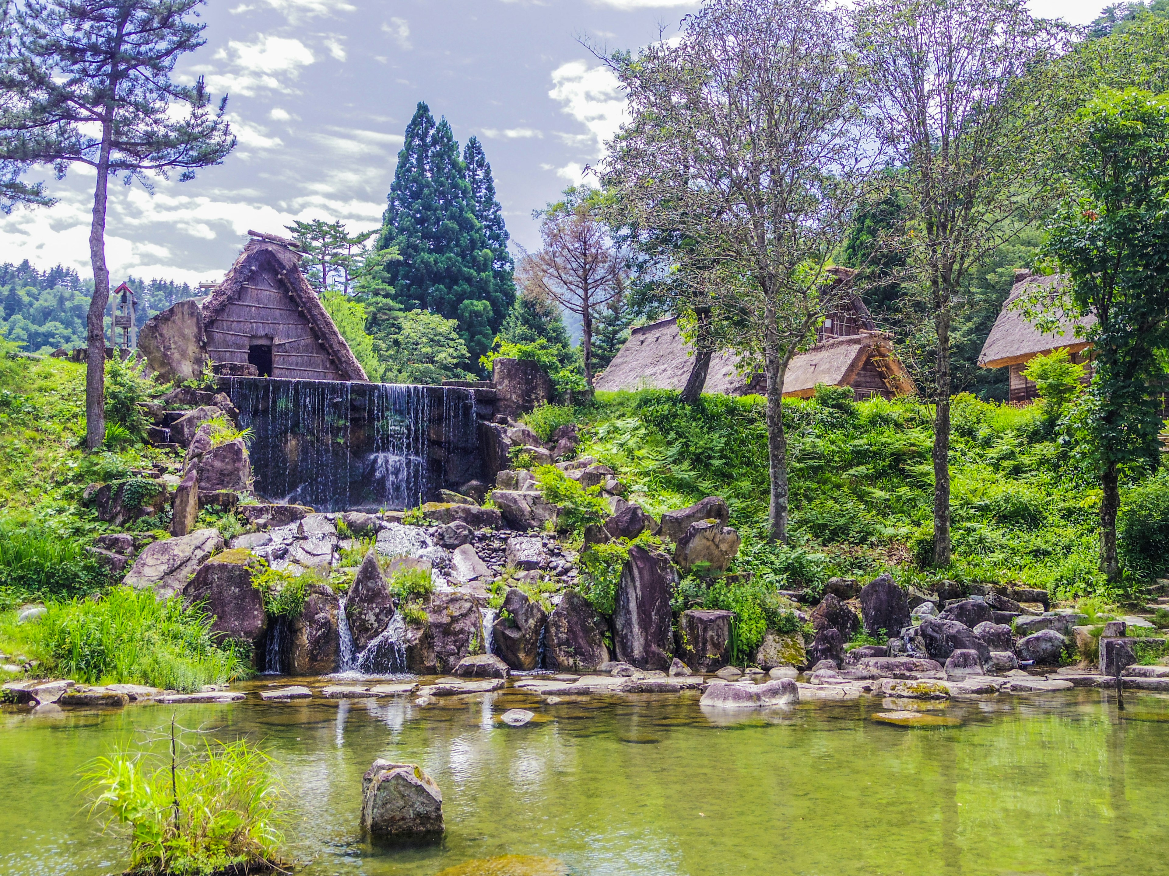 Pemandangan indah rumah tradisional dikelilingi oleh pepohonan hijau dan air terjun