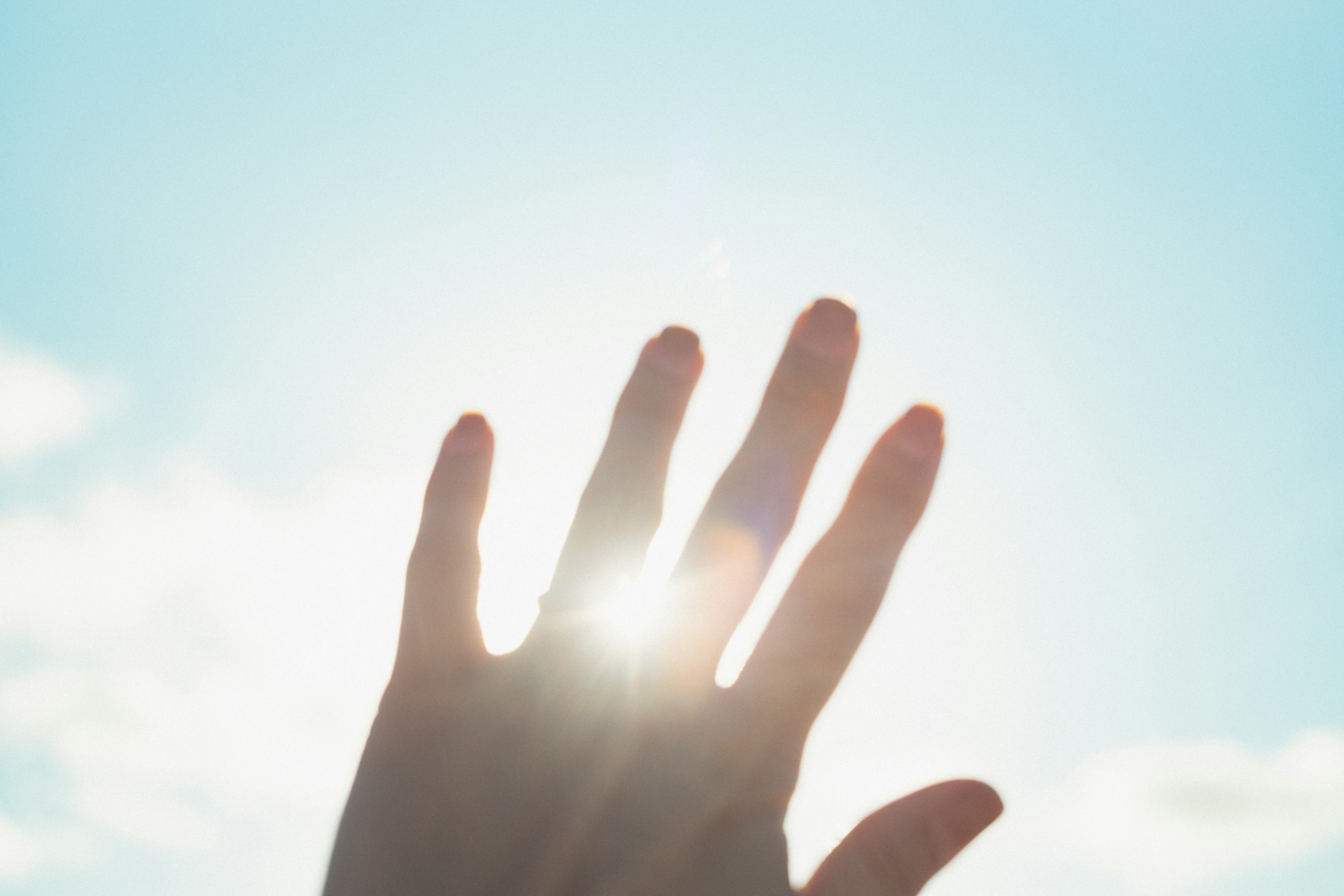 A person's hand blocking sunlight against a bright blue sky