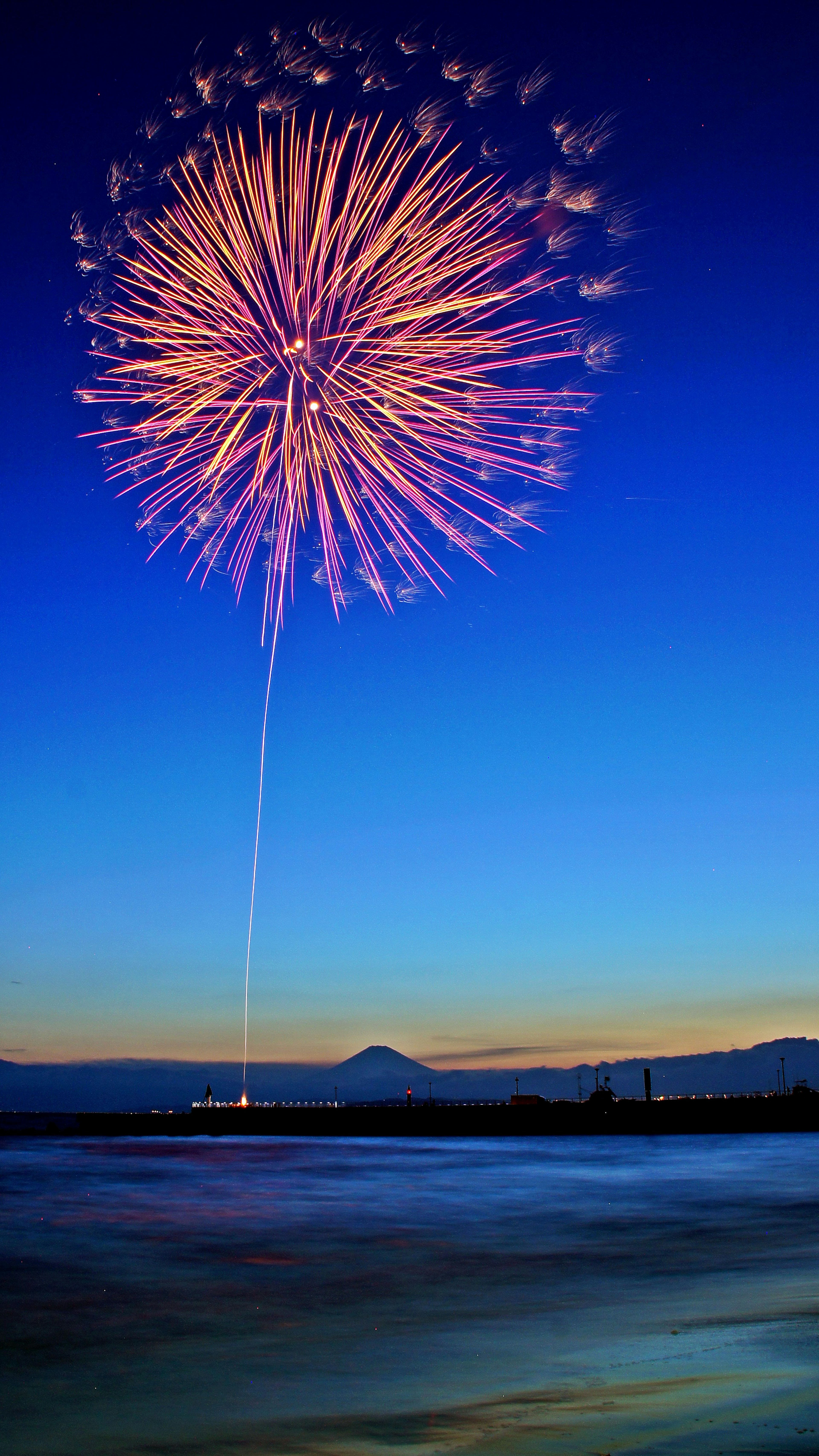 Fuegos artificiales coloridos estallando en el cielo de la tarde sobre un mar tranquilo