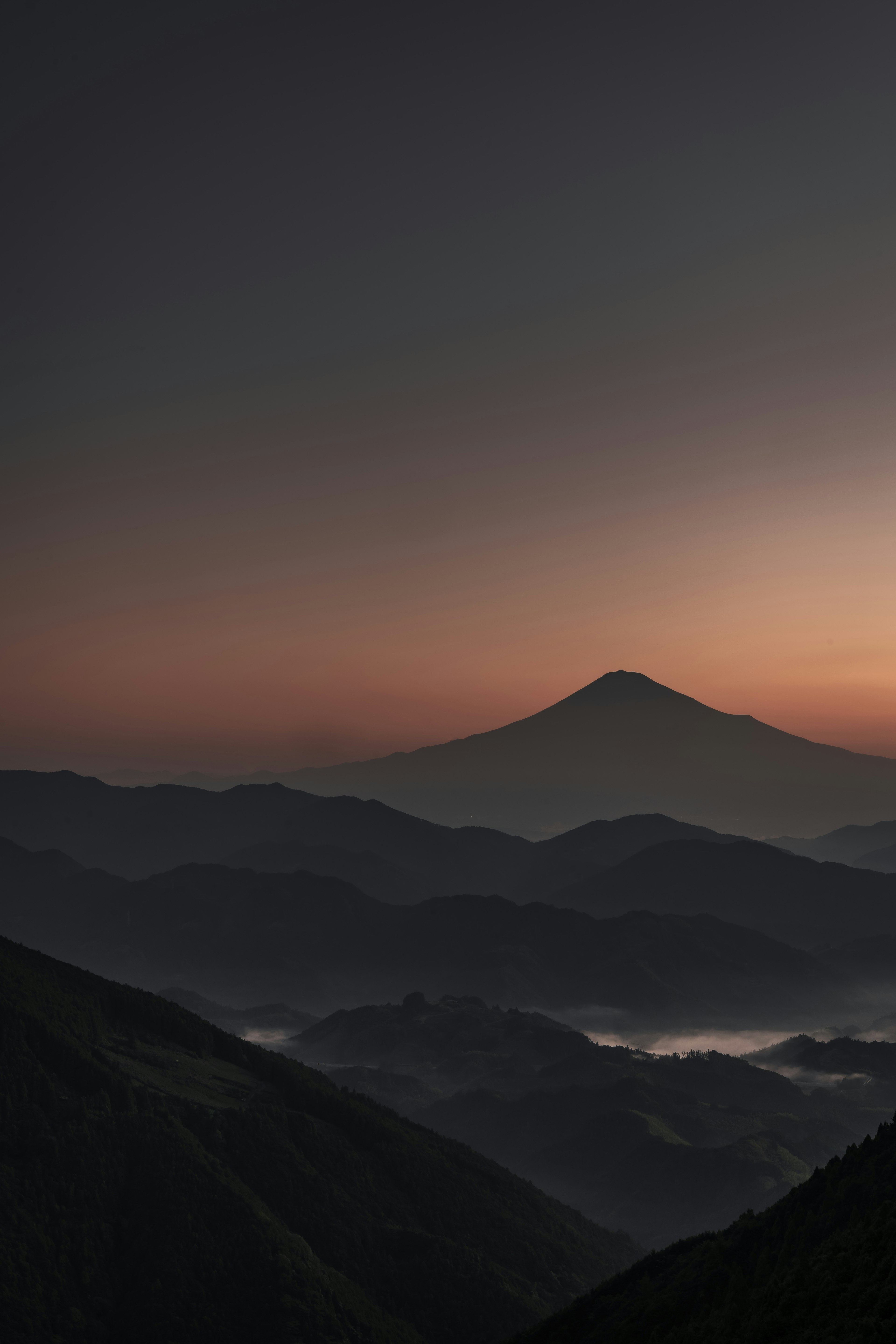 Un paisaje de montañas superpuestas al anochecer con un pico distante visible