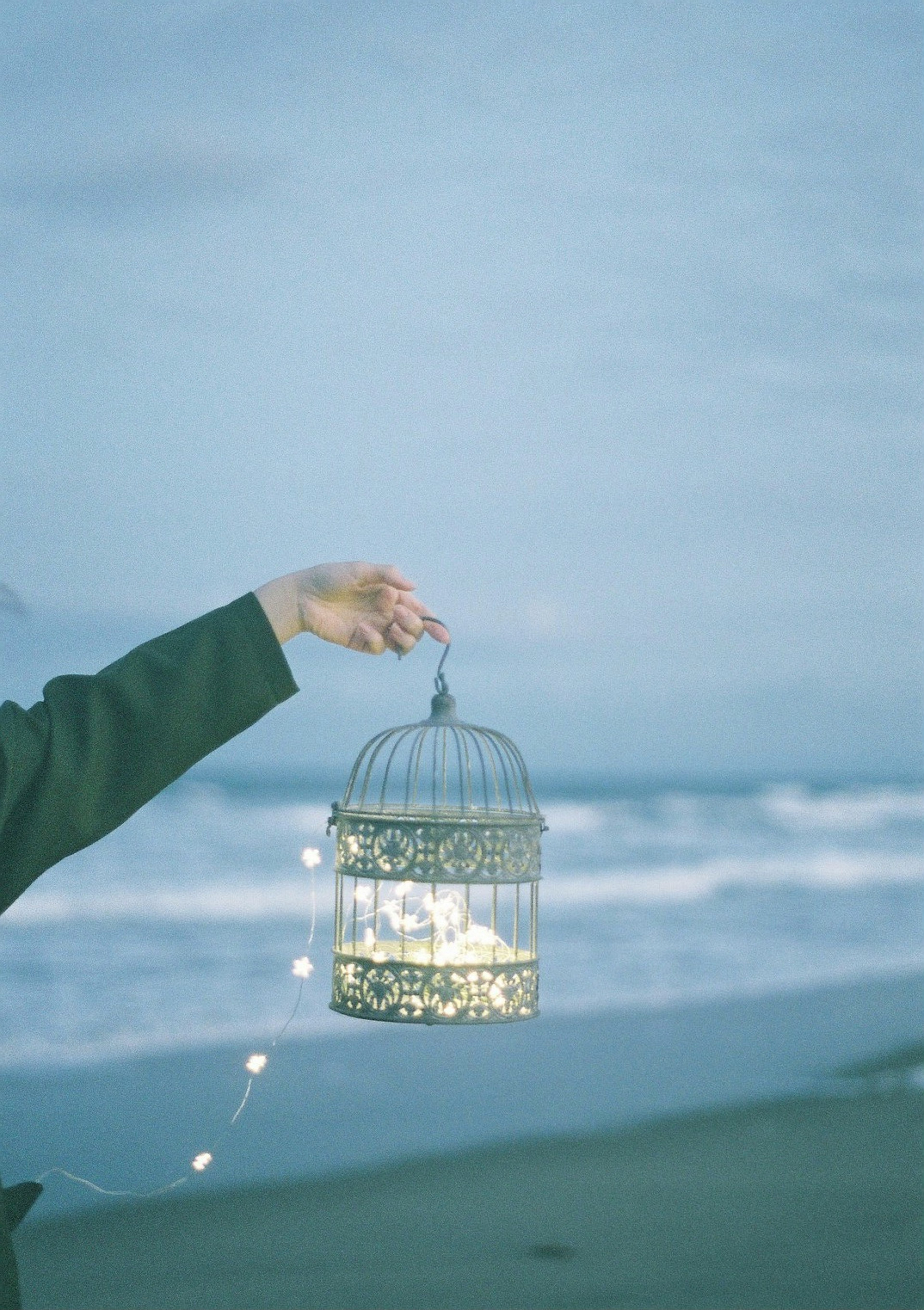 Une main tenant une cage à oiseaux illuminée au bord de la mer