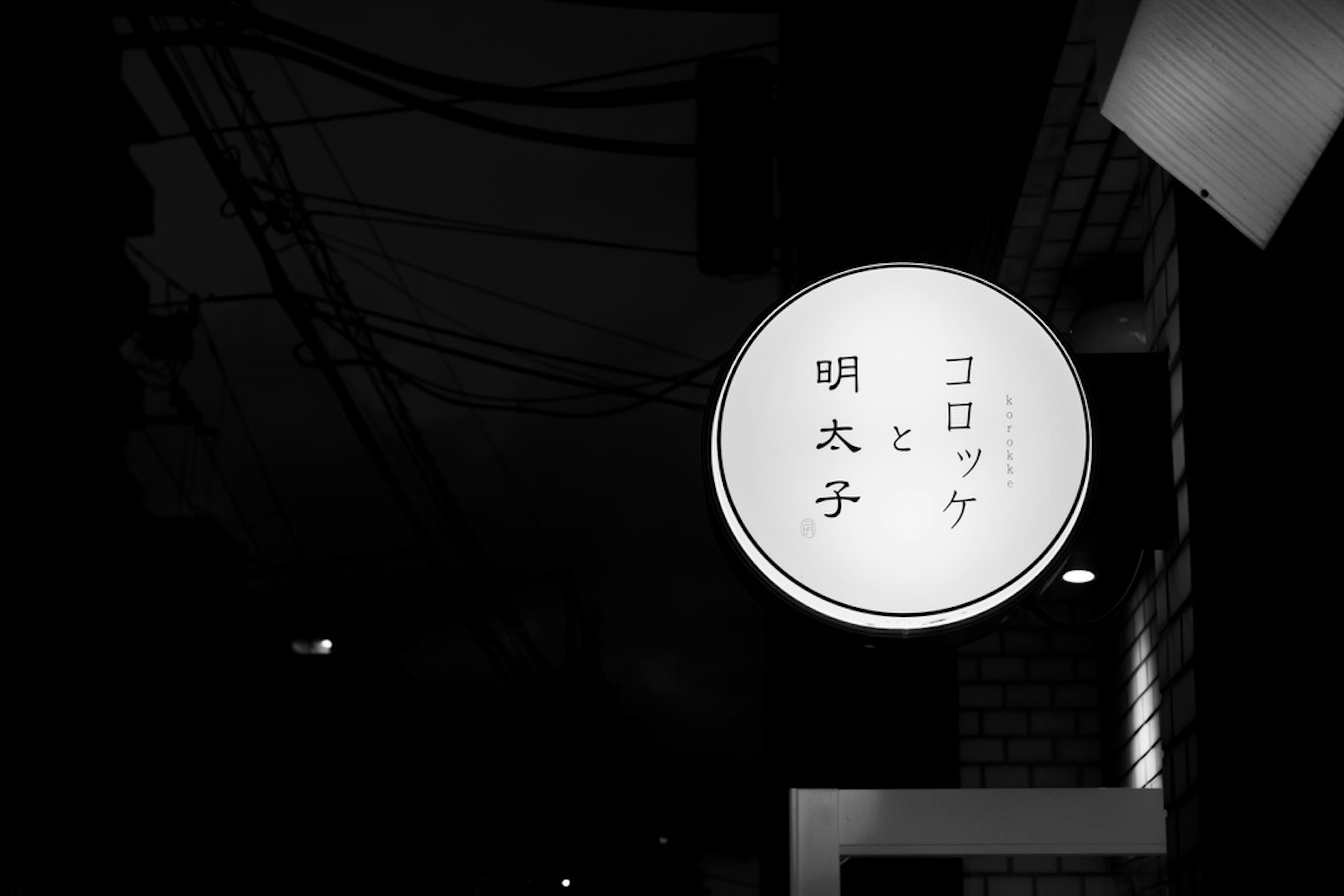 A round white sign with the text 明太子 and コロッケ against a dark background