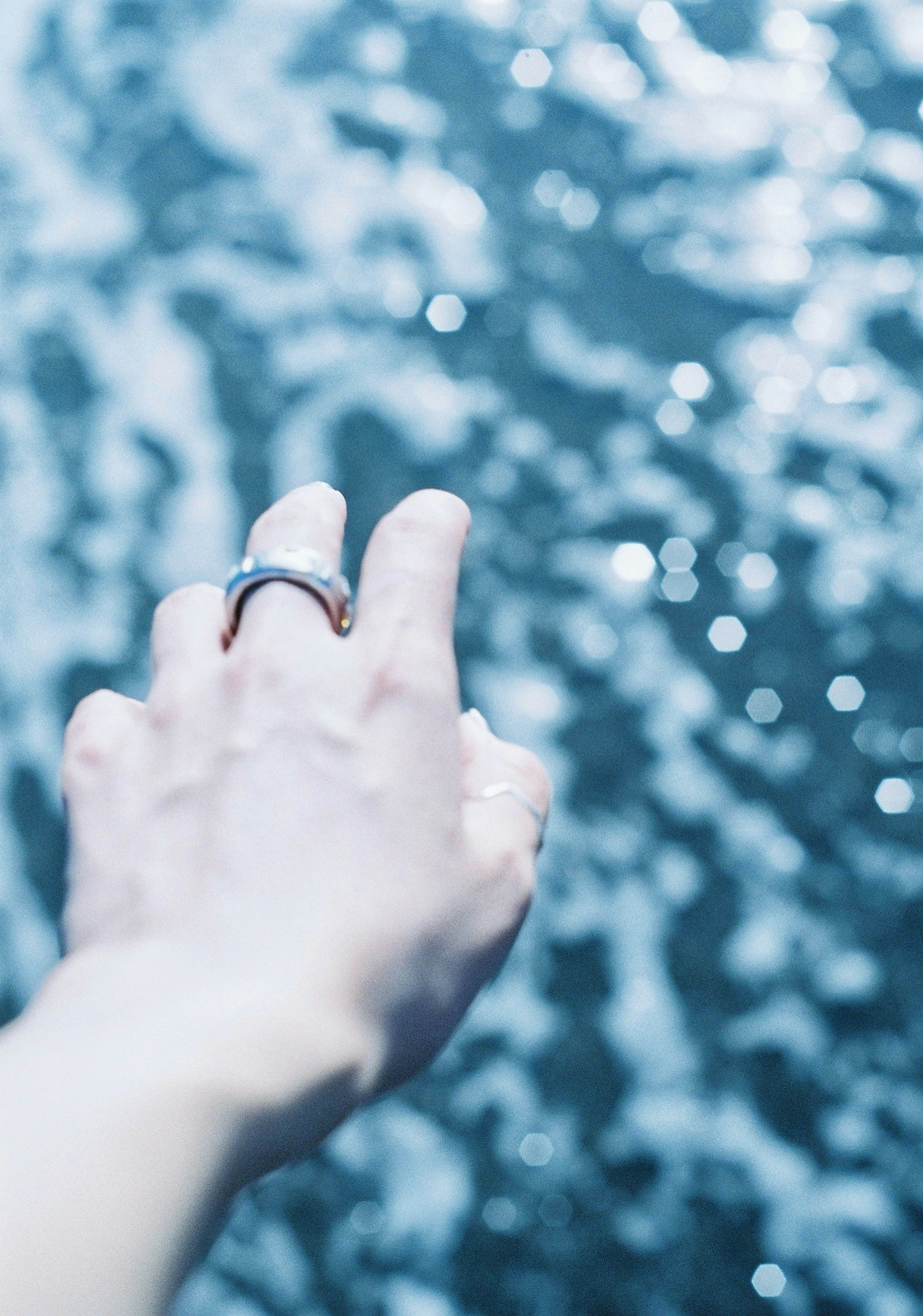 A hand reaching out towards rippling blue water with sparkling reflections