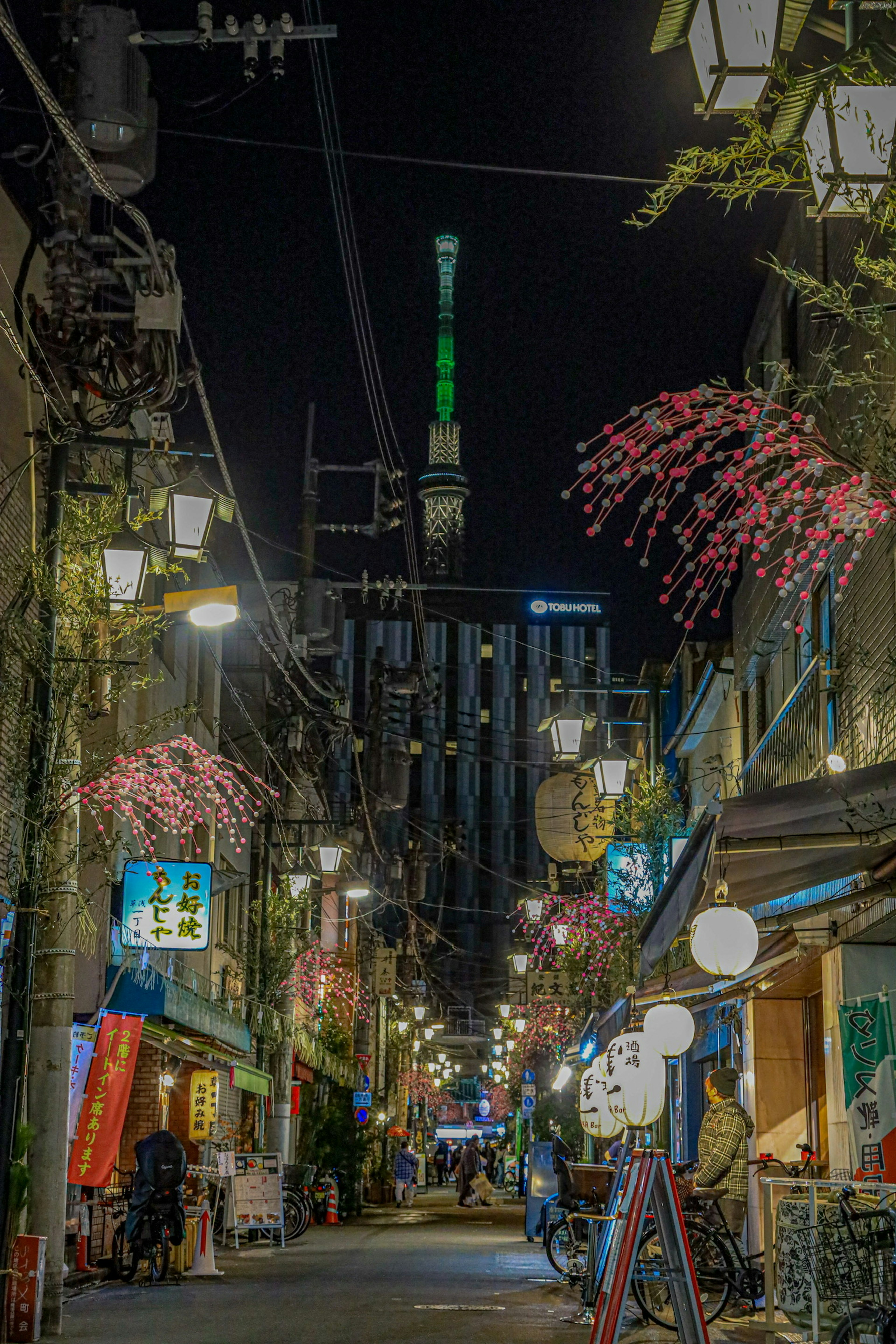 Narrow street in Tokyo at night lined with traditional Japanese lanterns and illuminated Tokyo Skytree in green