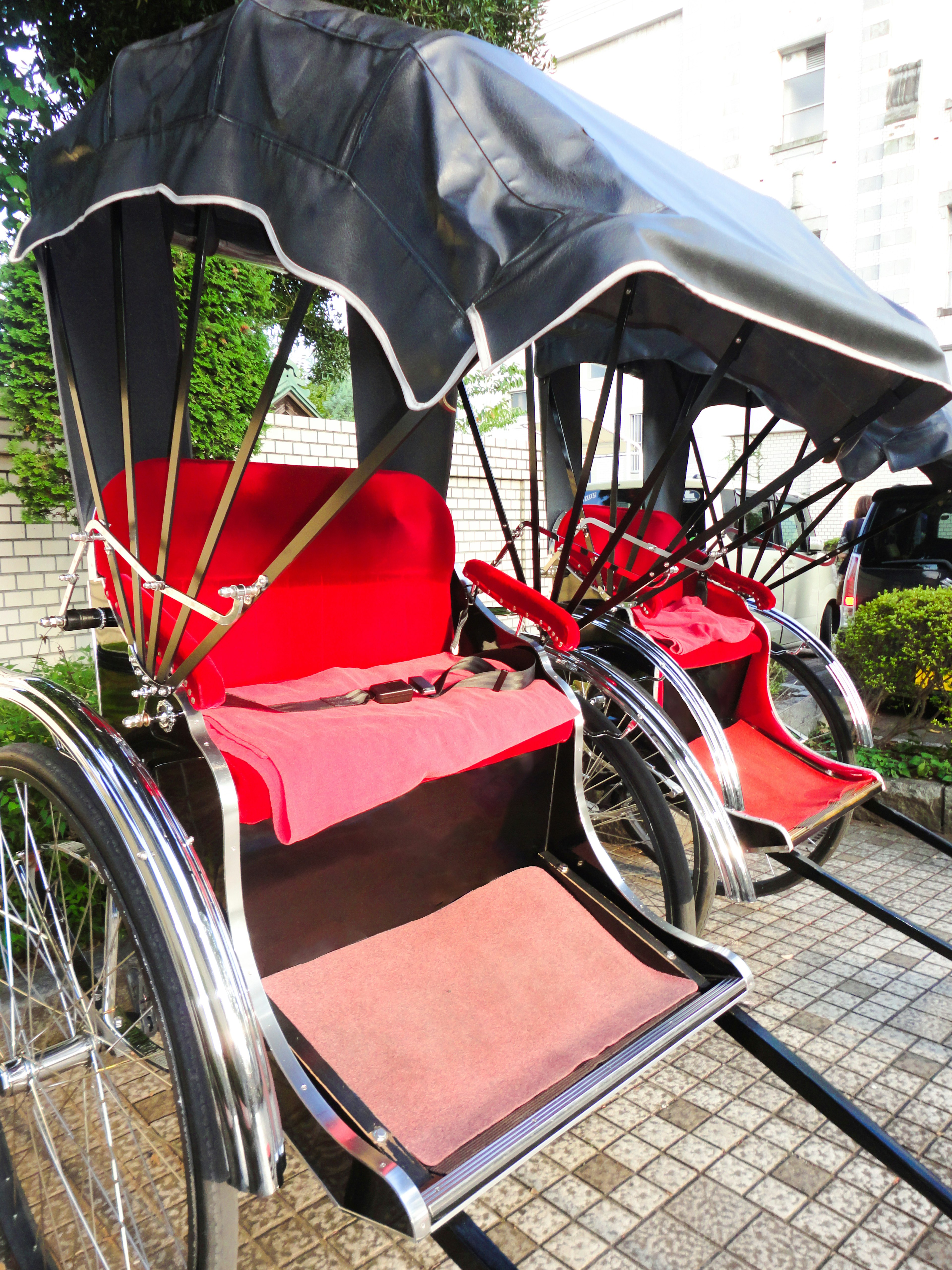 Two rickshaws with red cushions parked on a cobblestone path