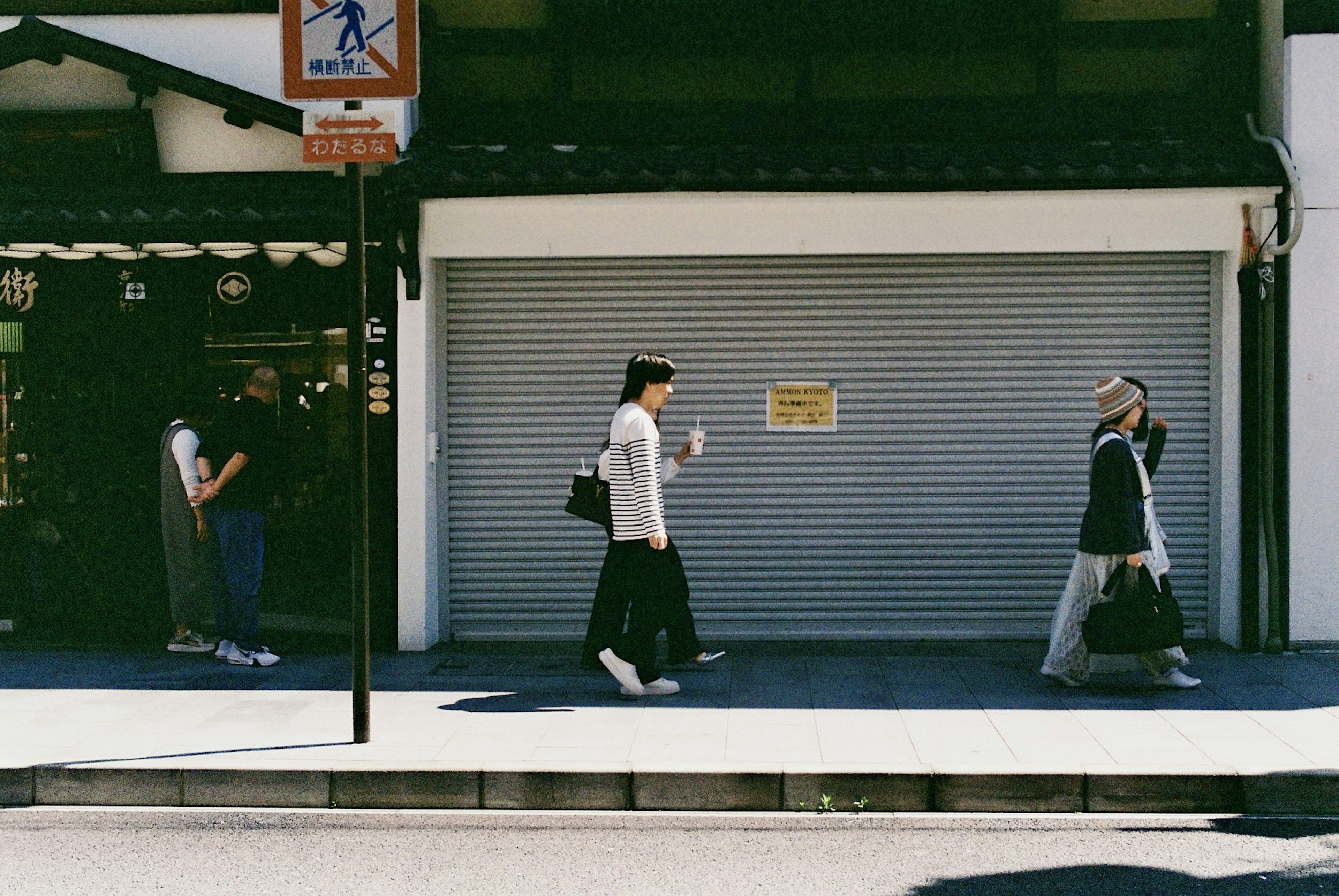 人們在安靜的街道上走過，商店捲簾門關閉