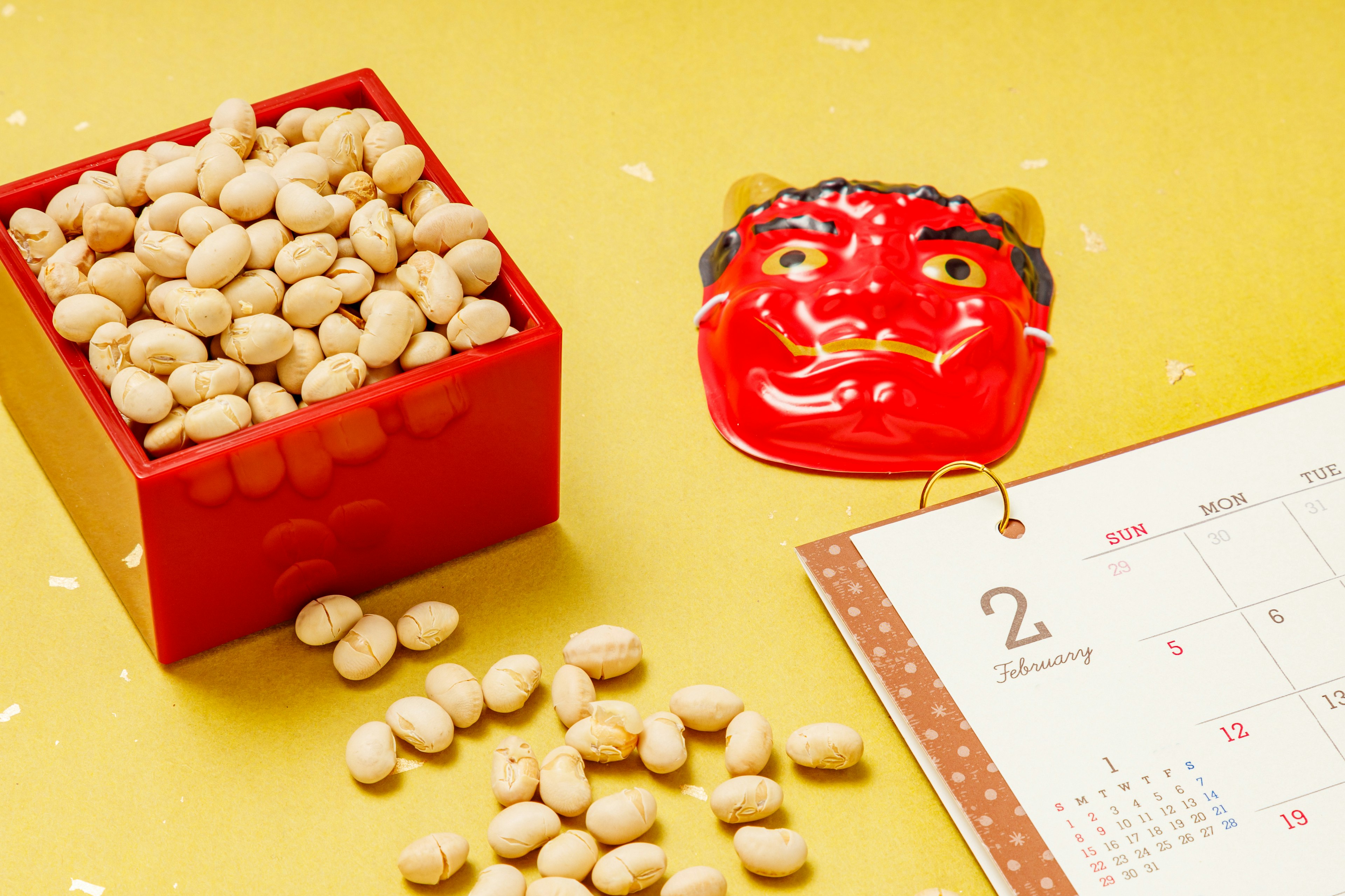 Red box filled with beans alongside a demon mask and a calendar