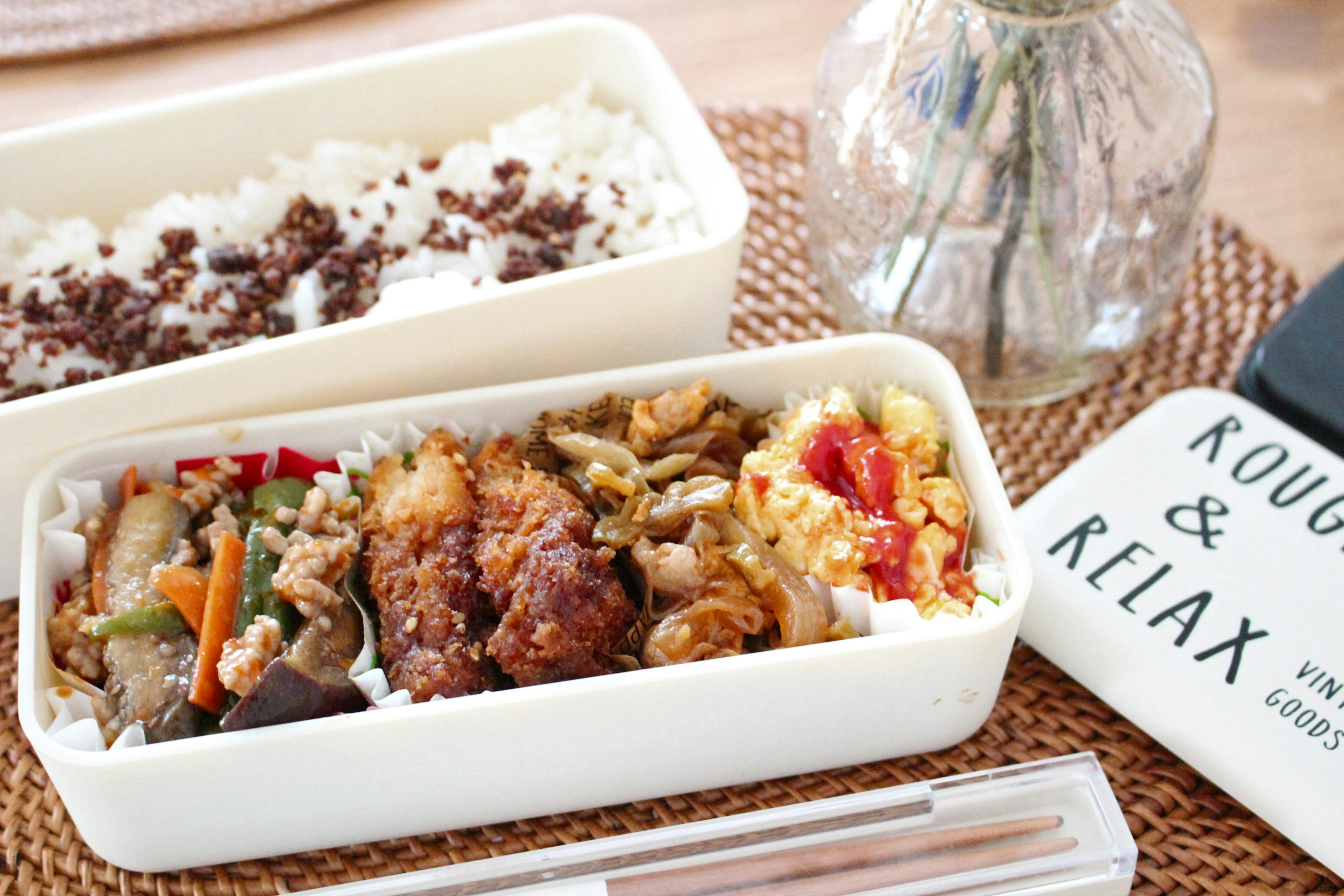 A bento box filled with chicken and vegetable dishes alongside rice